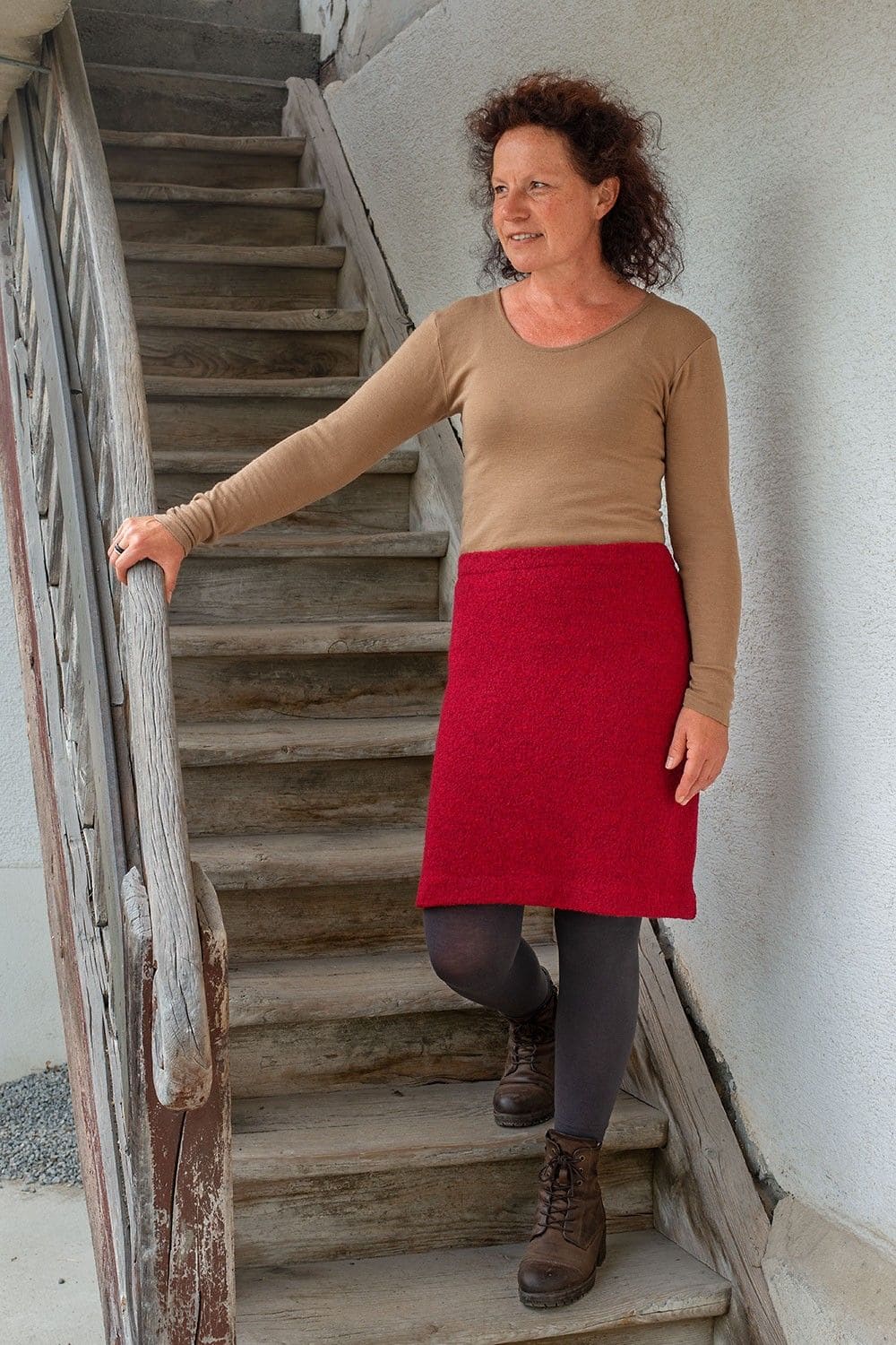 Frau kommt Treppe hinunter und trägt roten Wollkrepprock aus bio Wolle (kbT) mit beigem Shirt