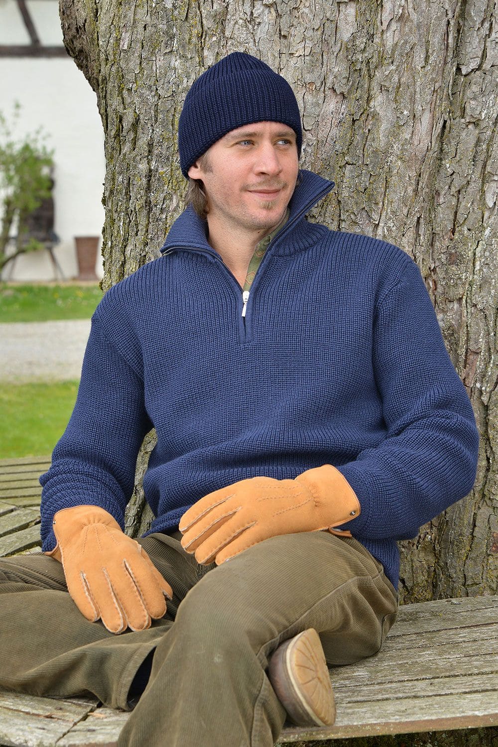 Mann sitzt auf einer Bank mit grüner Hose, Handschuhen, Pulli und blauer Wollmütze aus bio Wolle (kbT) vom Finkhof