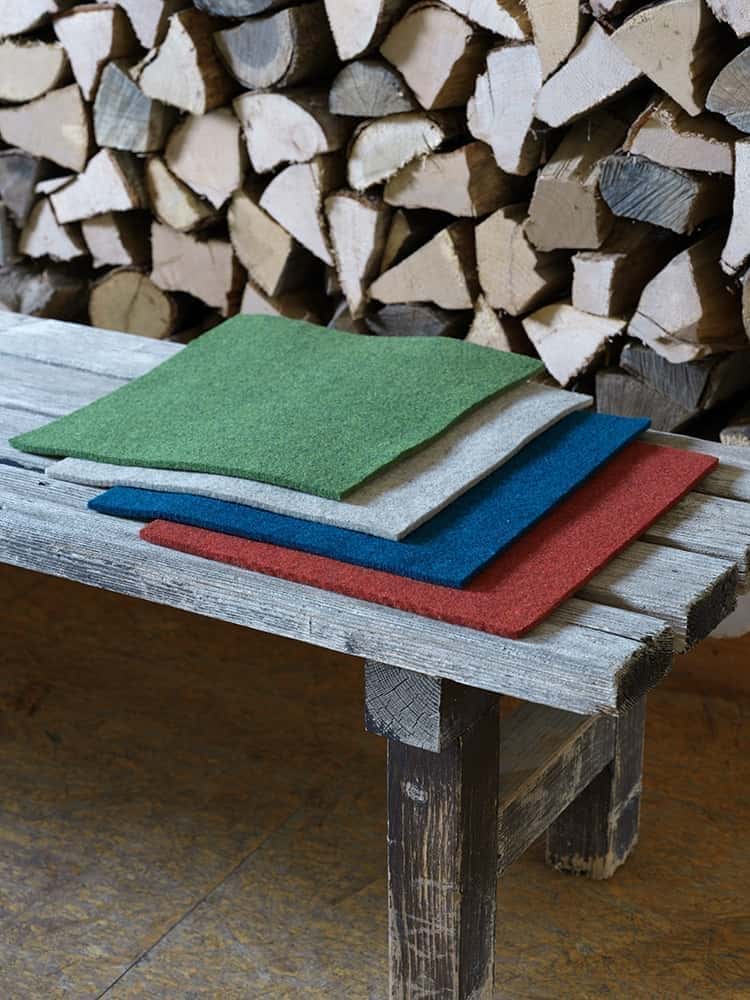 Quadratische Sitzauflagen aus Bio-Wolle vom Finkhof in verschiedenen Farben auf einer Holzbank