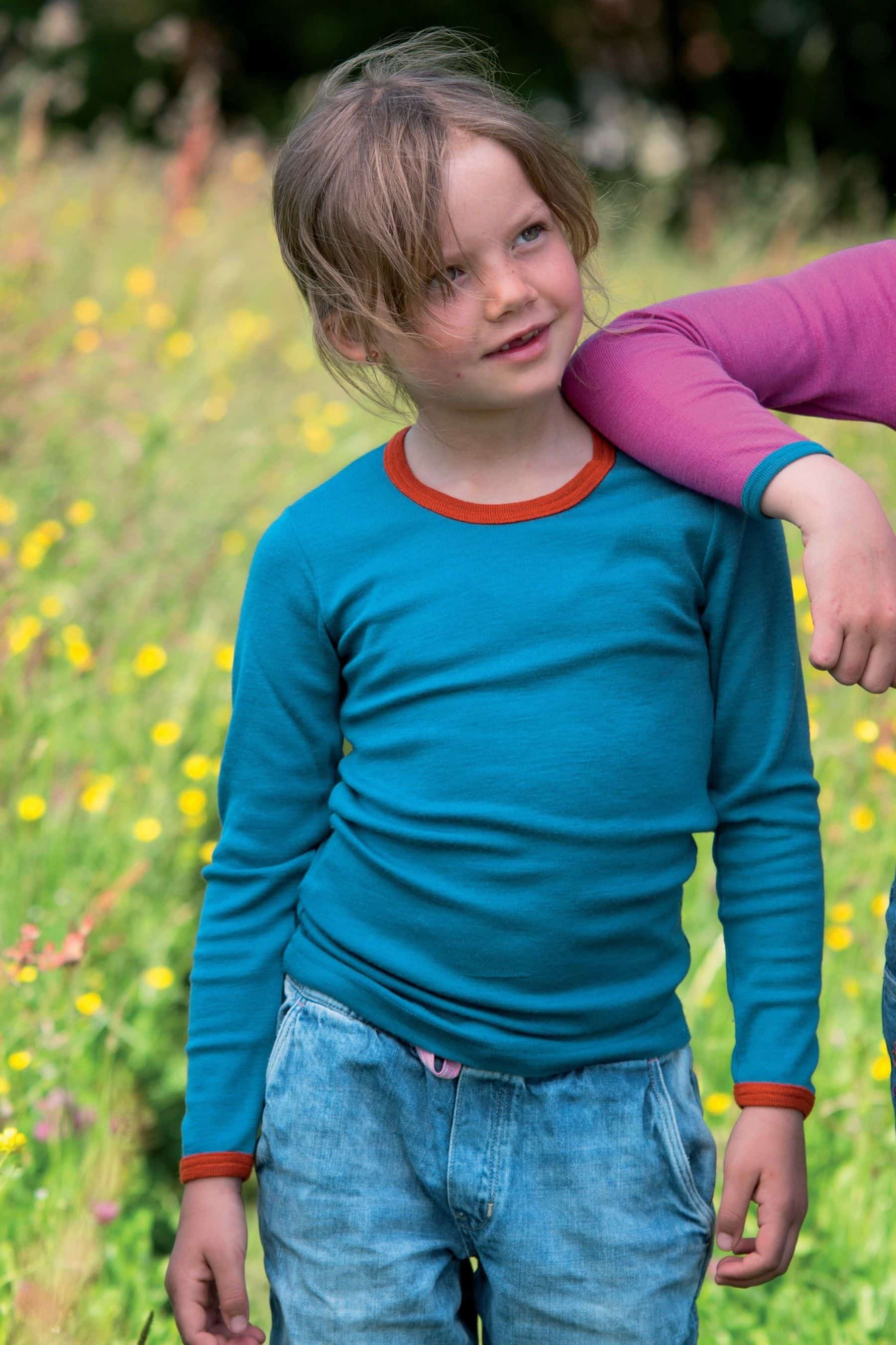 Mädchen trägt türkises Langarmshirt mit orangem Kragen aus bio Wolle (kbT) und Seide
