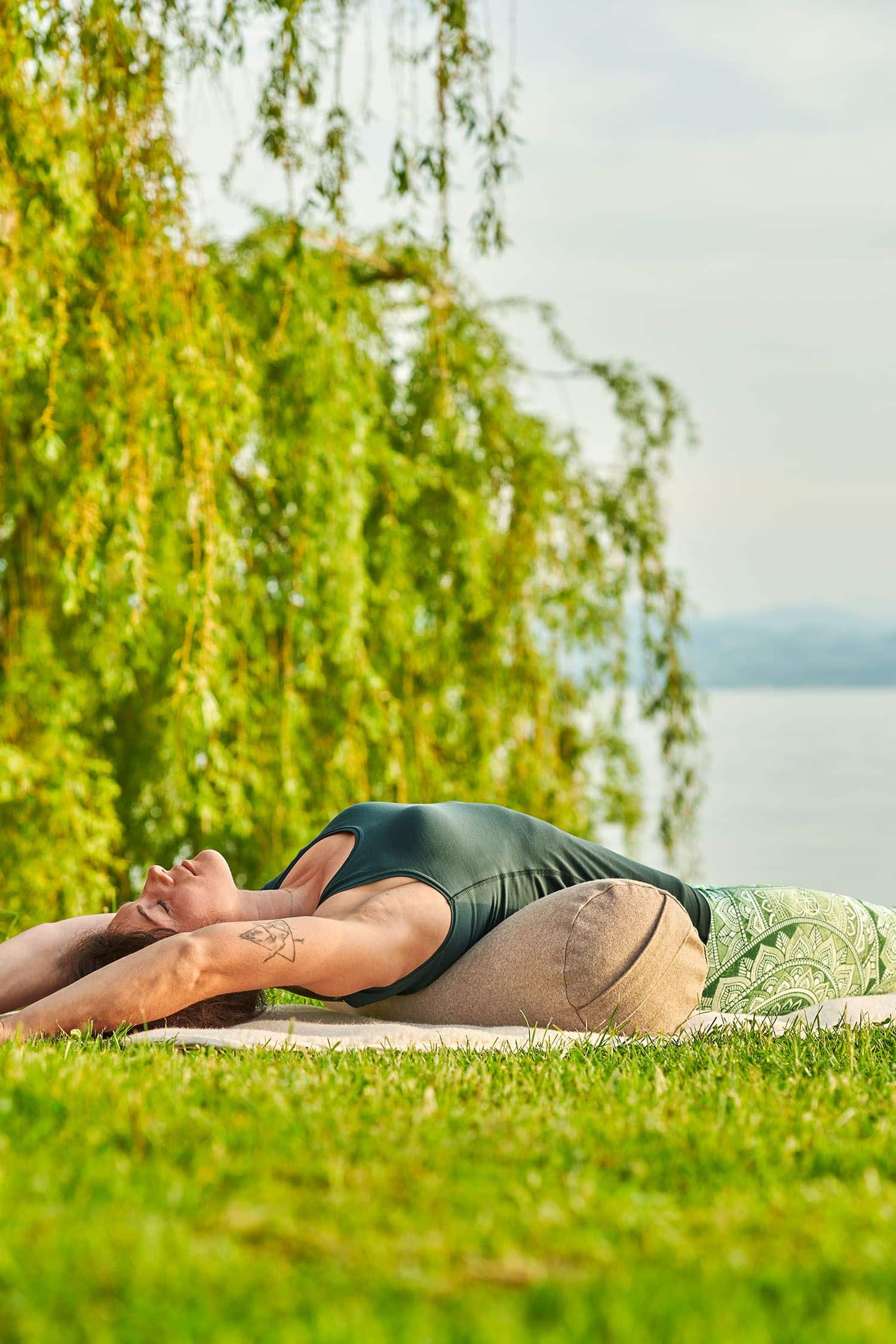 Frau liegt in grüner Yoga Kleidung auf einer hellen Meditationsrolle aus Loden mit Dinkelspelz gefüllt vom Finkhof