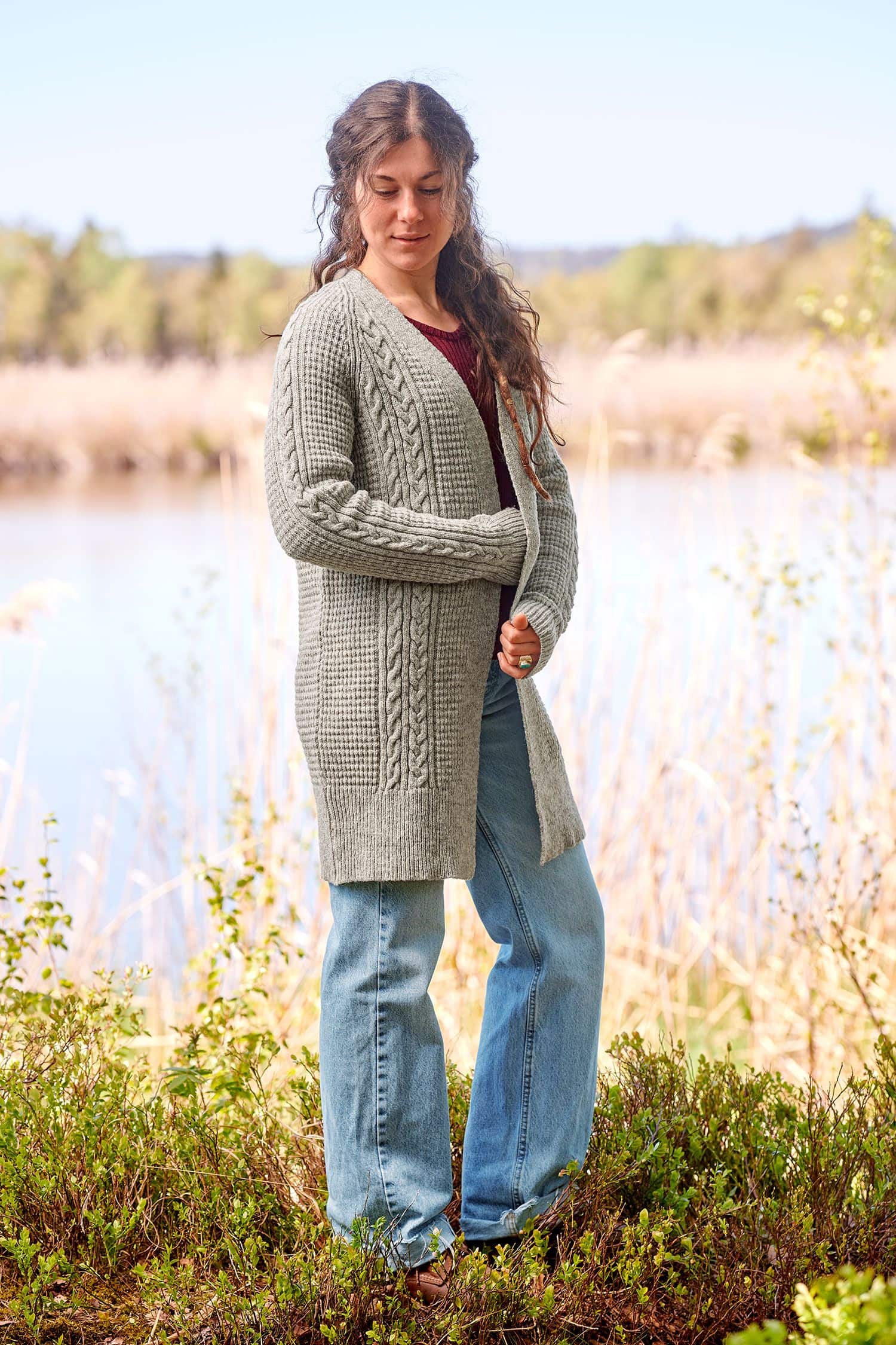 Frau mit Jeans trägt einen grauen ungefärbten Cardigan mit Zopfmuster aus bio Wolle (kbT) vom Finkhof, seitlich