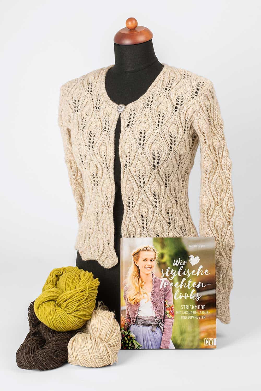 beige Strickweste an Puppe mit bunten Wollknäulen und dem Buch ,,Wir lieben stylische Trachtenlooks"