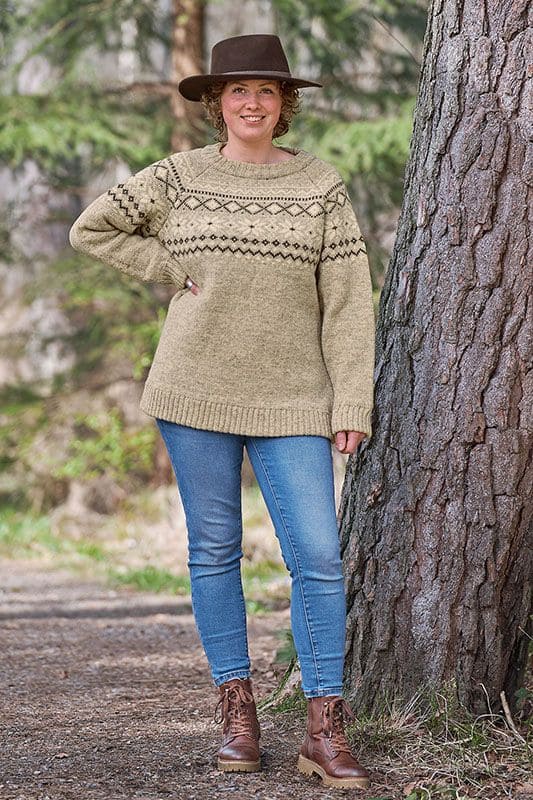 Finkhof-Norwegerpullover Frau mit Hut und Jeans steht neben Baum und trägt grauen Finkhof Norwegerpulli aus bio Wolle (kbT)
