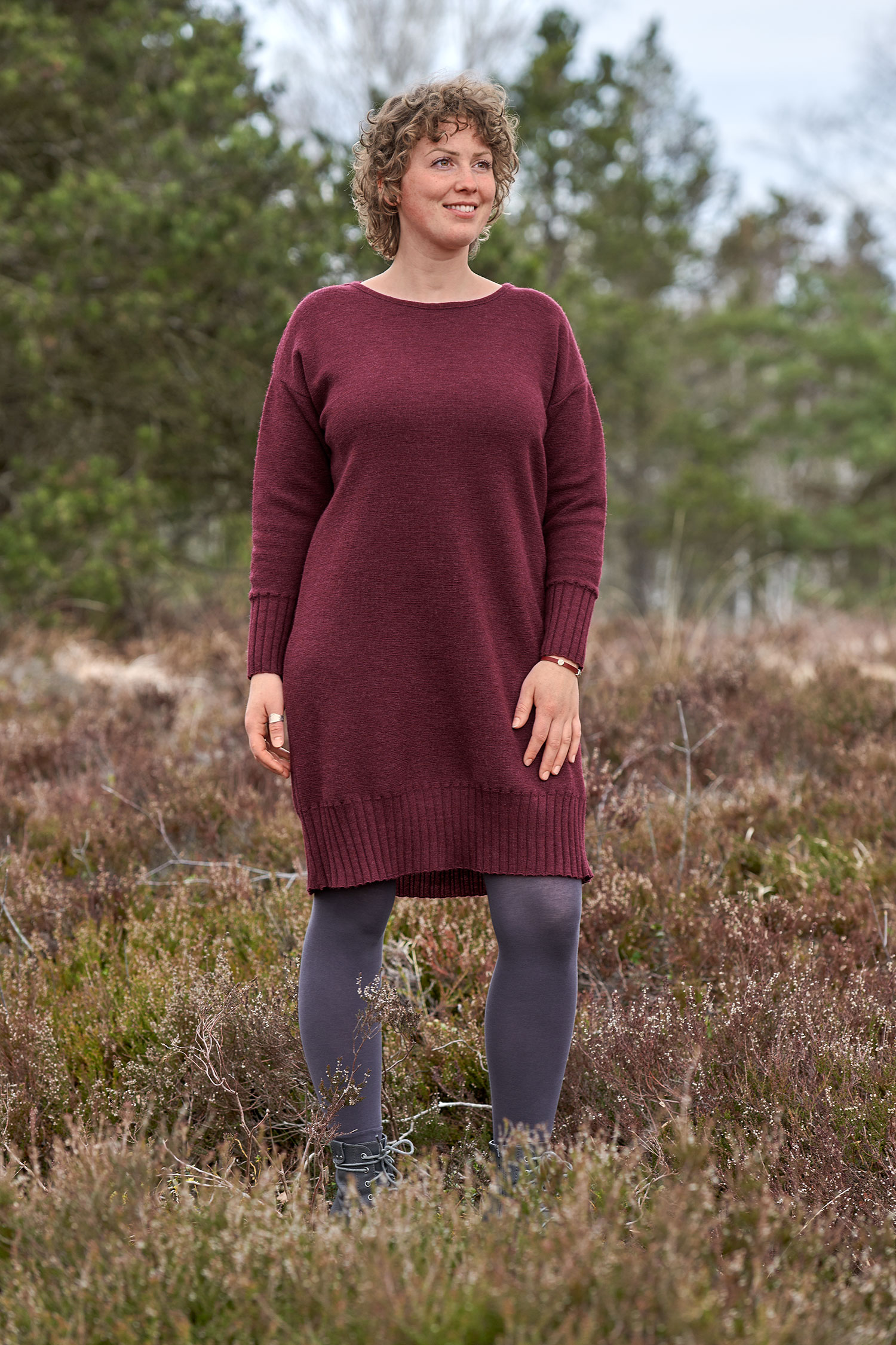 Frau trägt burgunderrotes Strickkleid aus bio Wolle (kbT) und eine bläuliche Strumpfhose