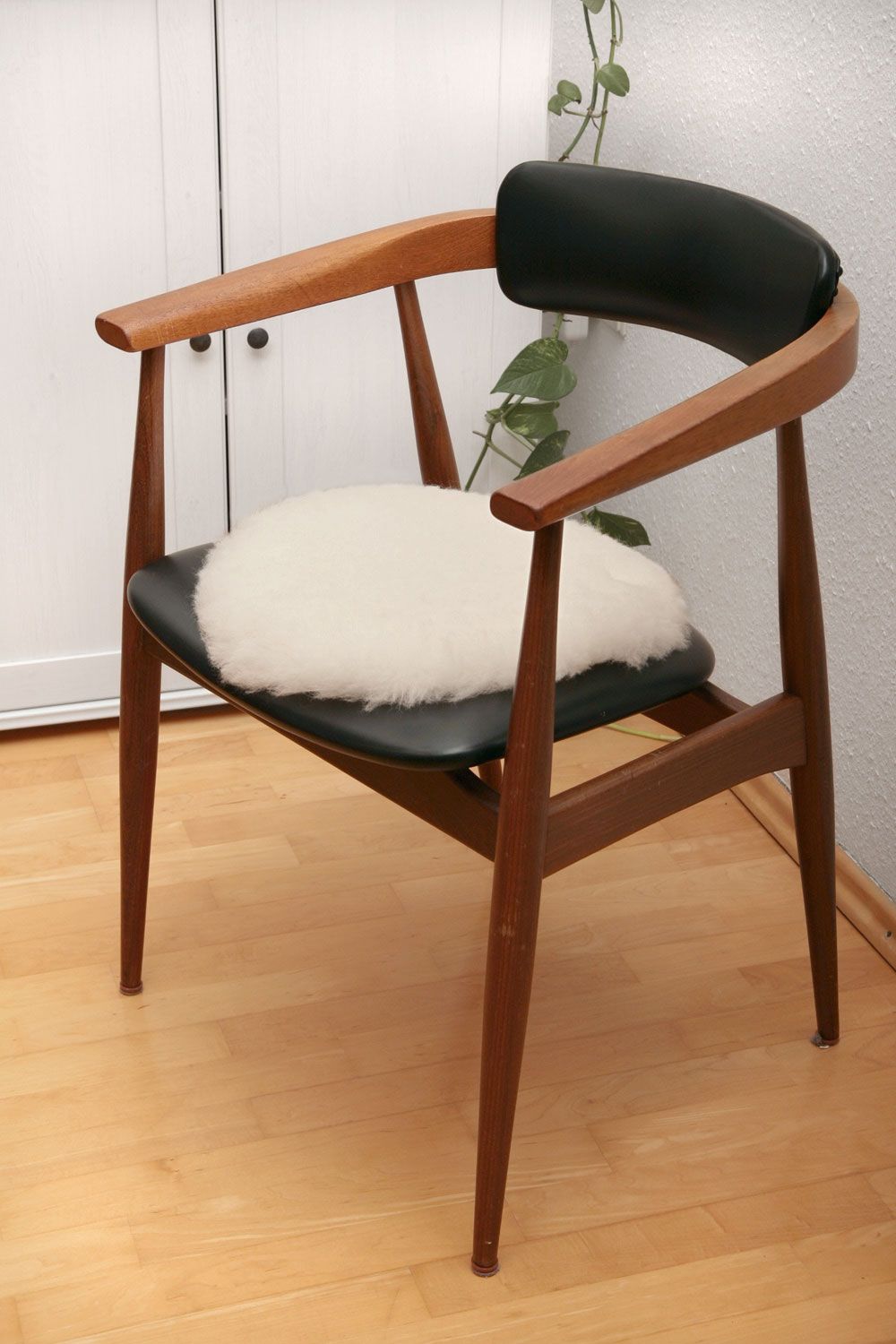 runde weiße Stuhlauflage aus pflanzlich gegerbtem Schaffell auf Holzstul mit schwarzer Fläche