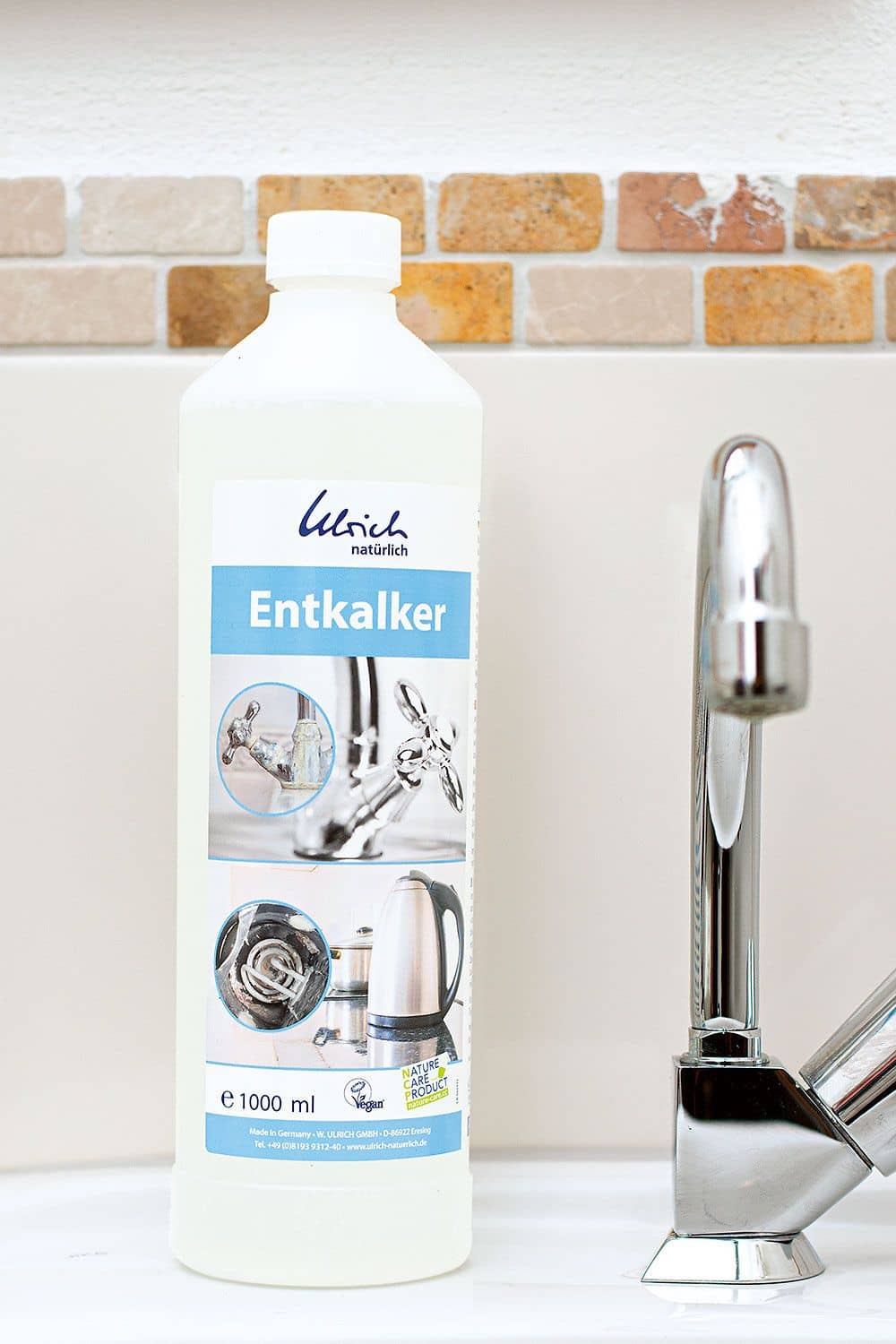 Flüssiger Entkalker 1000 ml Entkalker aus Milchsäure in 1000 ml Flasche mit weiß blauem Etikett vor silberner Waschbeckenamatur