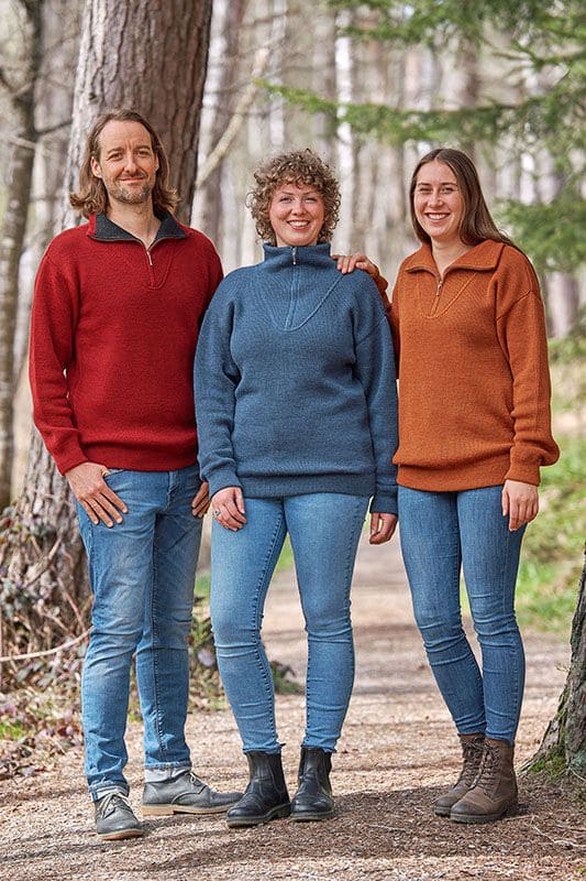 Troyer Mann und Frauen tragen Finkhof Troyer aus bio Wolle (kbT) mit Wald im Hintergrund