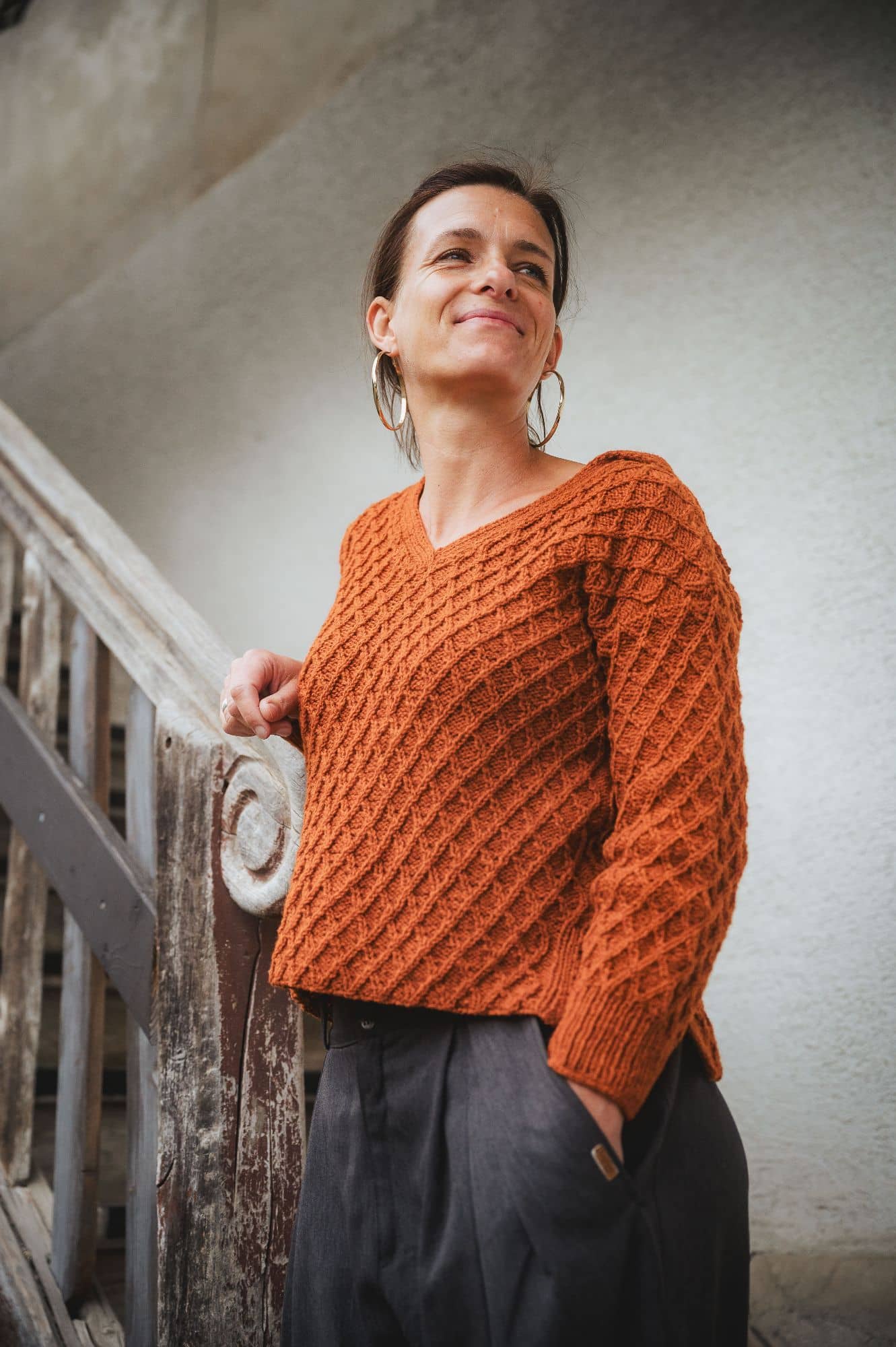 Frau steht an Treppe und trägt einen Strickpullover aus der dünnen bio Merinowolle (kbT) vom Finkhof in orangemeliert