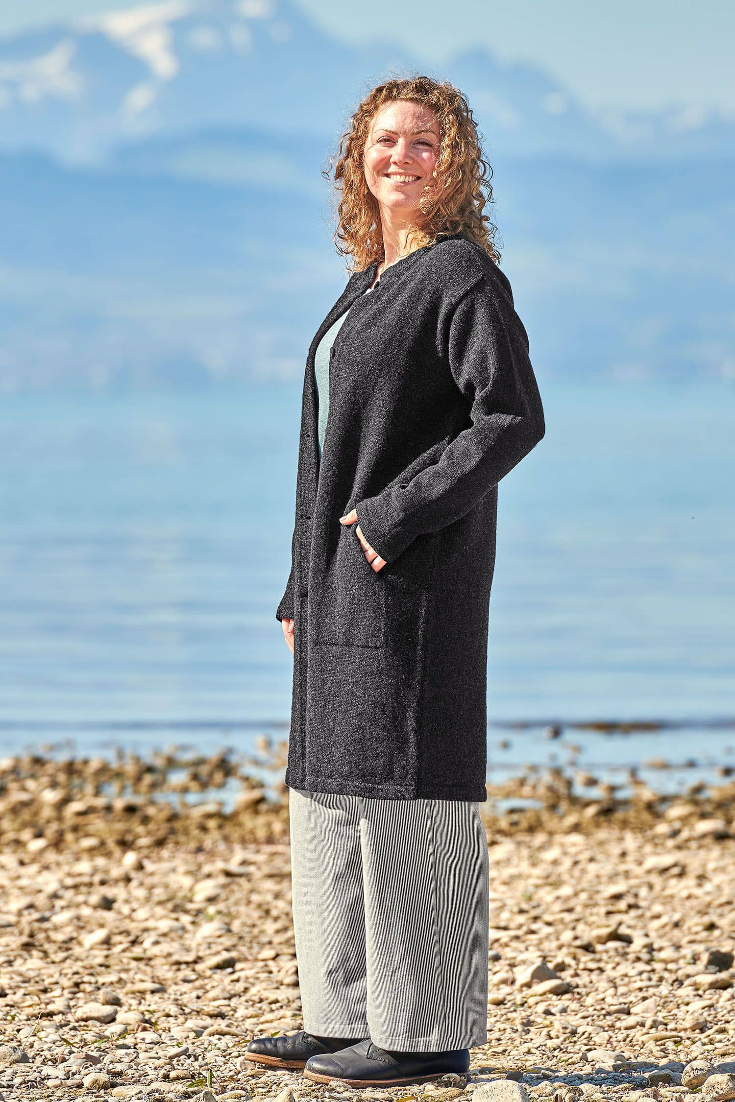 Frau trägt anthrazitgrauen Strickmantel aus bio Wolle (kbt) vom Finkhof, ein blaues Shirt und eine Stoffhose
