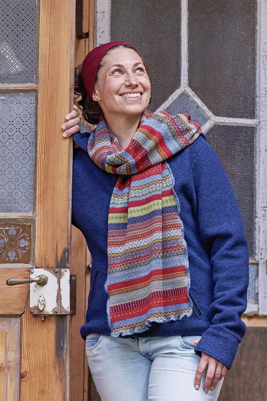 Schal Oslo Frau steht in Tür und trägt gemusterten Schal aus Wolle, blauer Strickpulli und rotes Stirnband