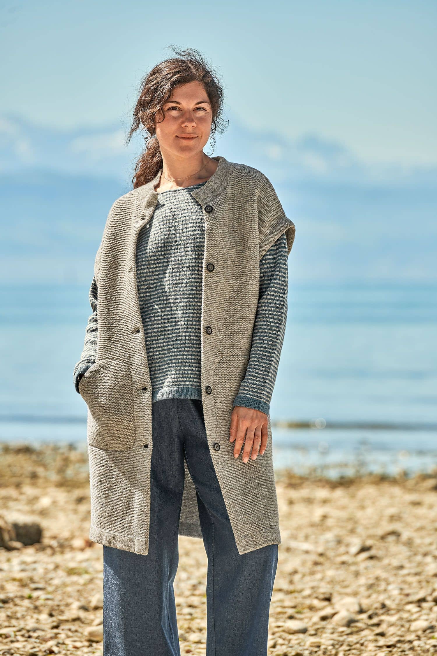 Finkhof-Damenstrickweste lang grau Gr. M Frau trägt blauen Streifenpullover und eine graue lange Strickweste vom Finkhof aus bio Merinowolle (kbT)