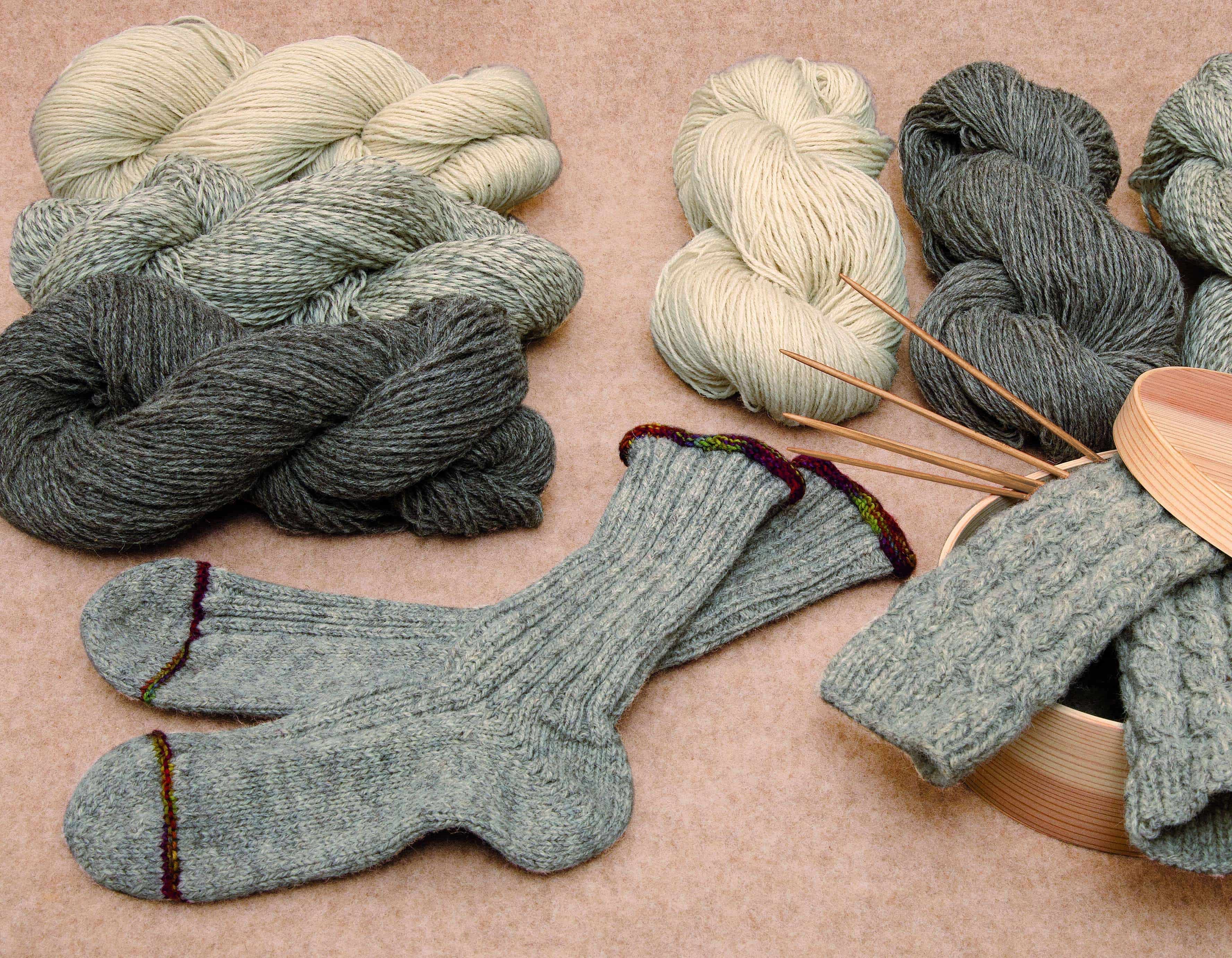 Bild mit grauer Stricksocke und ungefärbten Wollen im Hintergrund