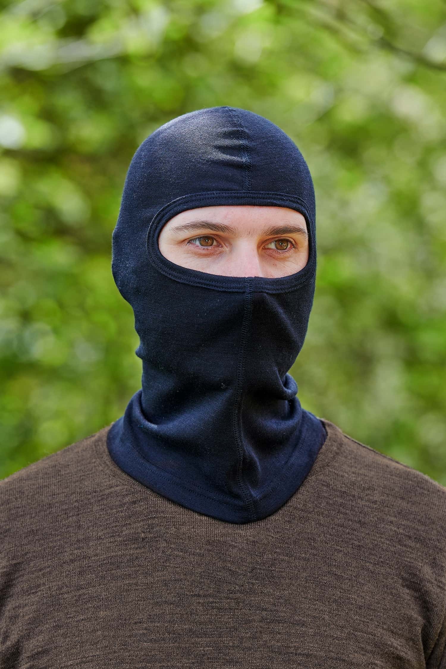 Mann mit braunem Pullover trägt eine schwarze Sturmhaube aus Bio-Schurwolle und Seide