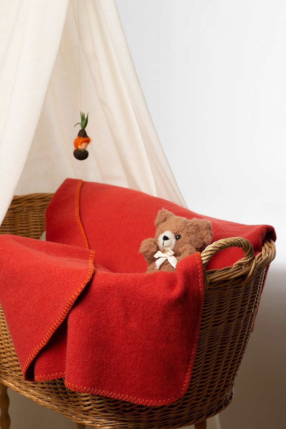 rostrote Kinder Wolldecke aus bio Wolle (kbT) vom Finkhof liegt in einem Stubenwagen mit Teddybär