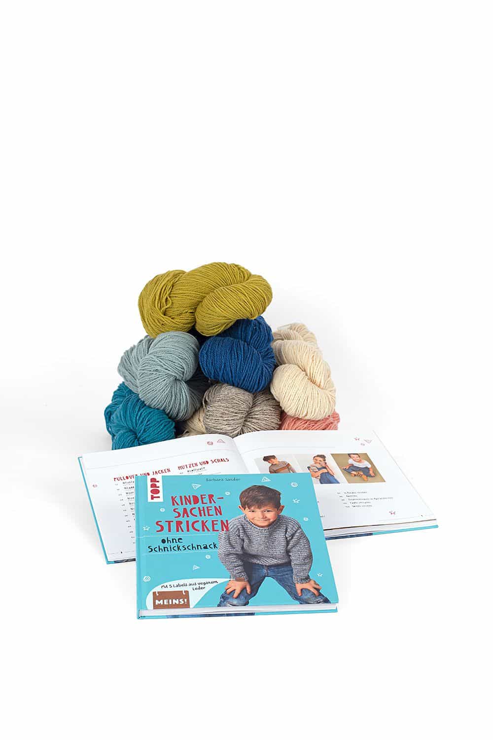 Kindersachen stricken ohne Schnickschnack Buch ,,Kindersachen stricken ohne Schnickschnack" liegt auf aufgeschlagenem Exemplar und Wollknäulpyramide im Hintergrund