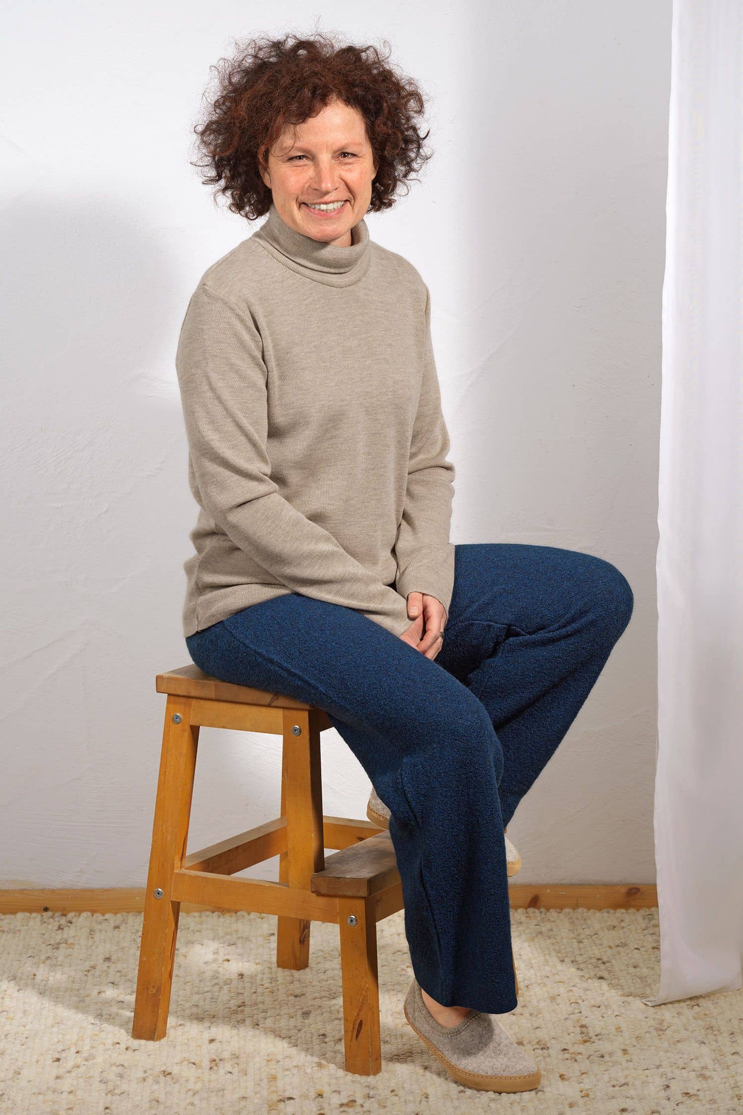 Damen-Wollkrepp-Hose marine Gr. S Frau sitzt auf Hocker und trägt eine marineblaue Wollkrepphose aus bio Wolle (kbT) und einen beigen Pullover