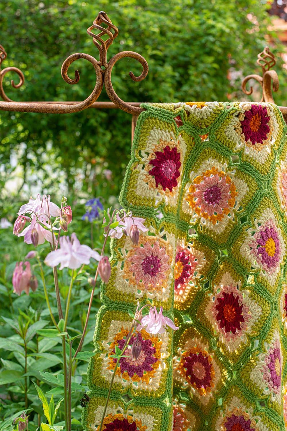 Patchworkdecke in grün und pink aus dem Buch ,,Wunderschöne Häkeldecken" über einer rostigen Stange im Garten