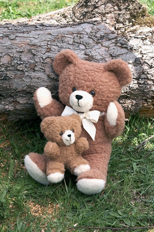 Wolltier Großer Bär brauner großer Wollbär hält kleiner Wollbär, vor Baumstamm sitzend