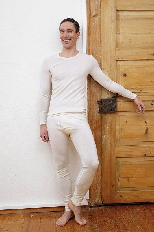 Lange Wollunterhose Herren naturweiß Mann lehnt an Wand mit Tür und trägt naturweiße lange Wollunterhose aus bio Wolle (kbT) mit passendem Shirt