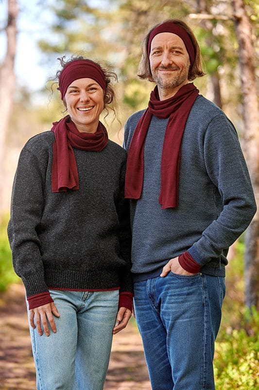 Mann und Frau mit dunklen Pullis tragen bordeauxrote Stirnbänder, Schals und Pulswärmer aus bio Wolle (kbT) und Seide