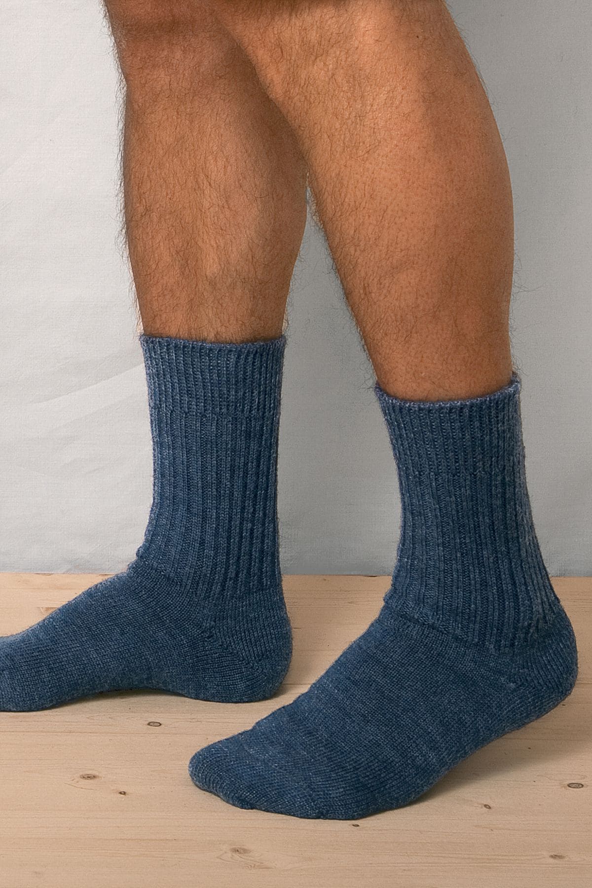 Person steht auf Holzboden und trägt jeansblaue Wollsocken aus bio Wolle (kbT) in mittlerer Dicke, von der Seite