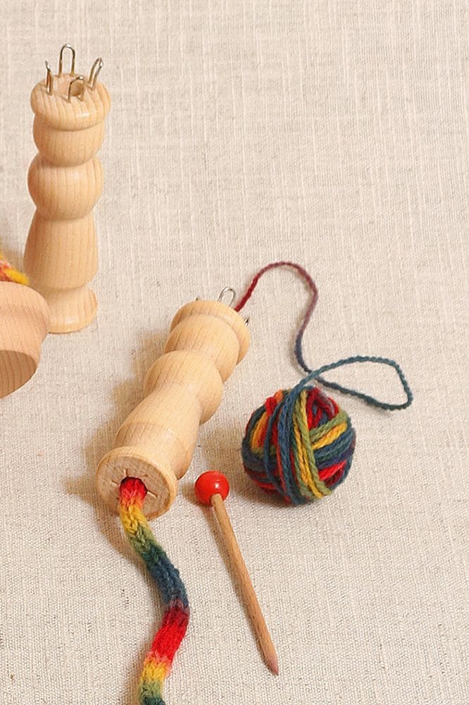 Strickliesel Strickliesel aus Holz liegt mit buntem Strickstück auf beigem Untergrund daneben steht eine weitere Strickliesel aus Holz