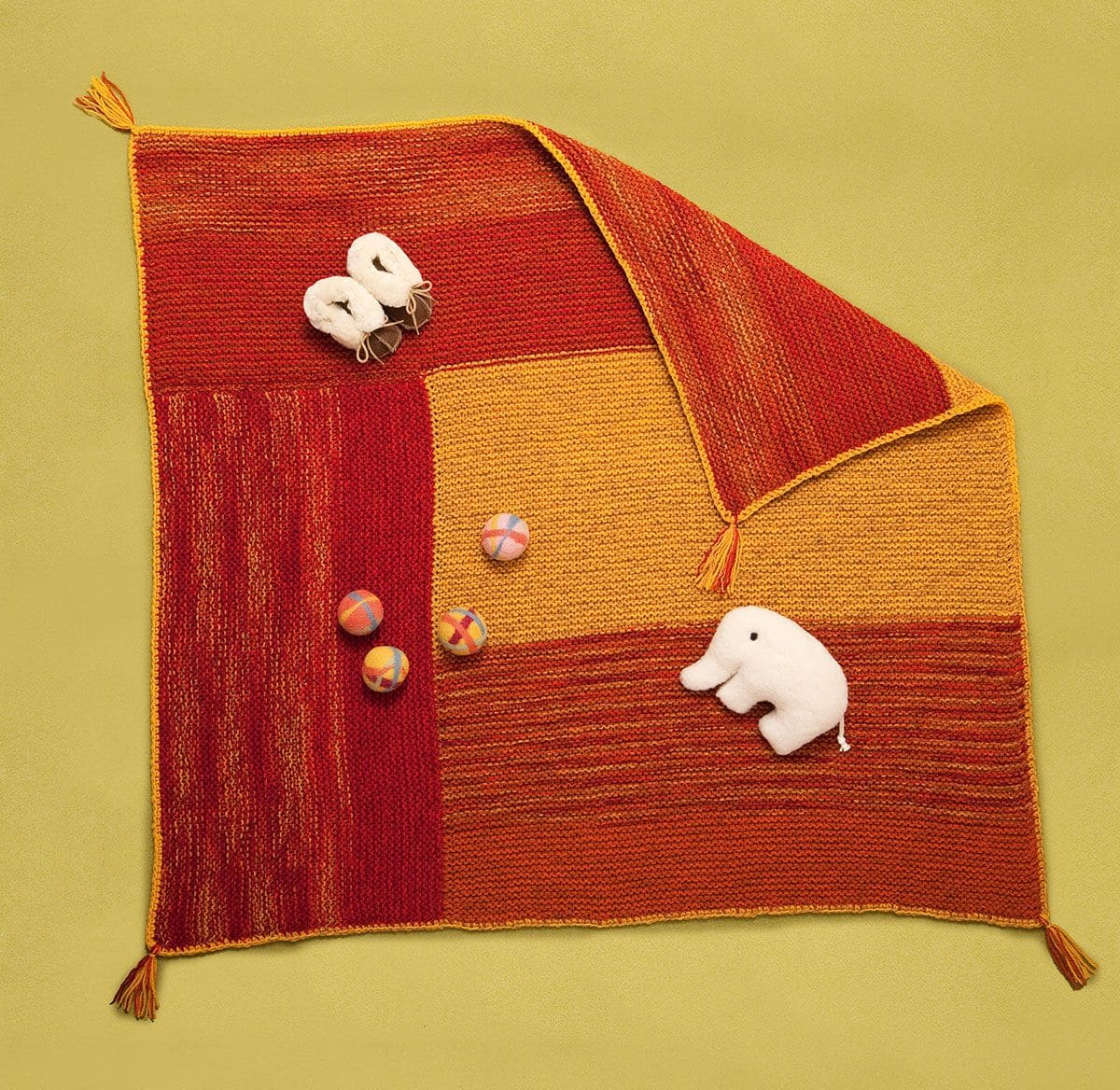 orange rote Strickdecke mit Fellschuhen, Filzkugeln und Plüschelefant mit Anleitung