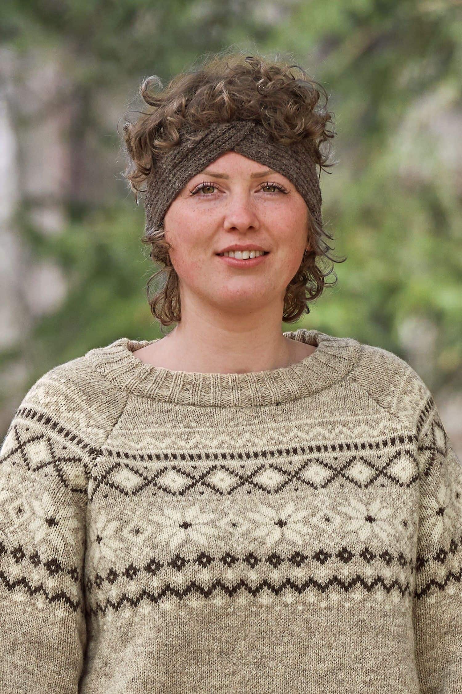 Finkhof-Stirnband Twist braun Frau mit hellbraunem Norwegerpulli trägt ein braunes Stirnband mit Twist aus bio Wolle (kbT) vom Finkhof