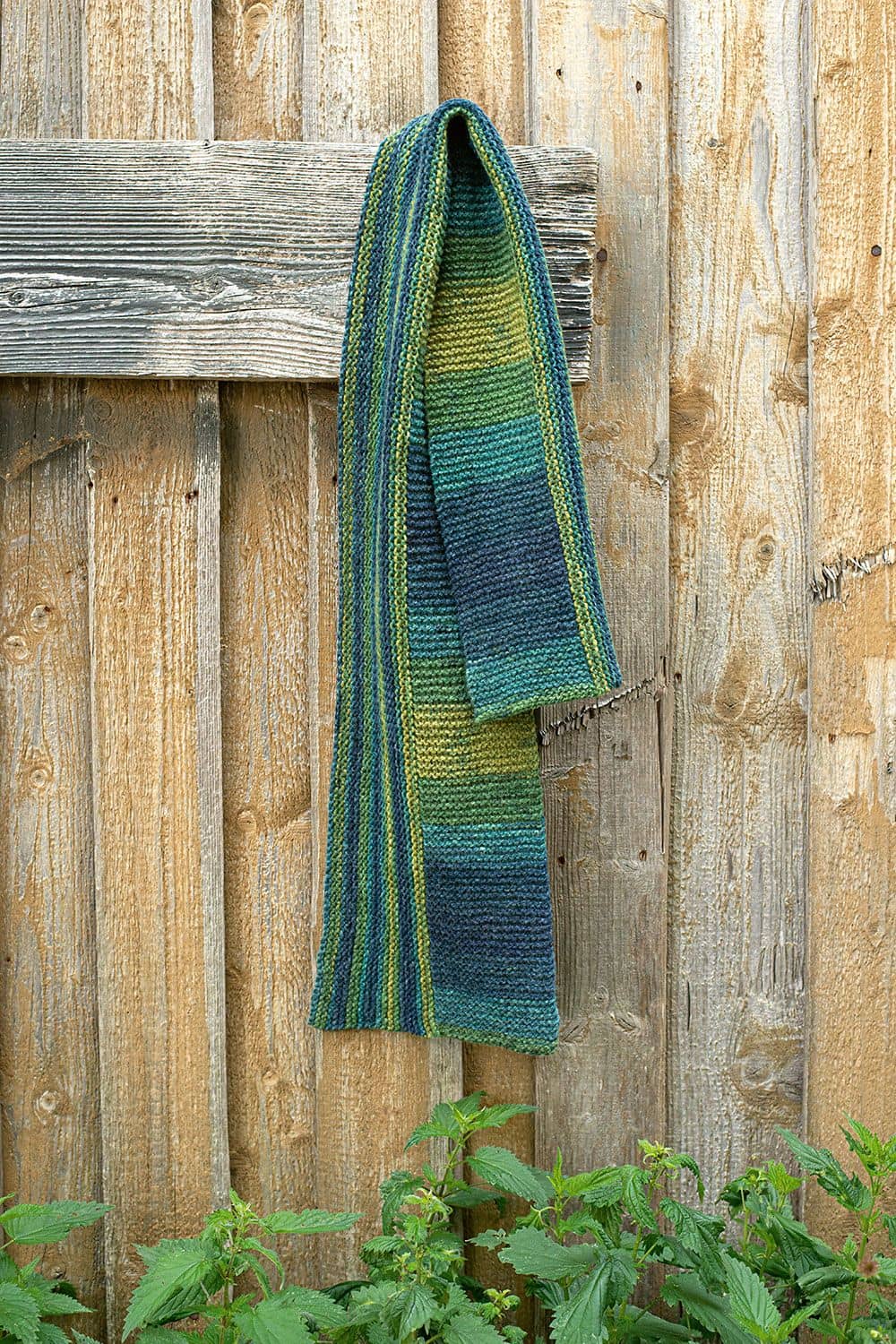 ein blau grün gemusterter Schal aus bio Merinowolle (kbT) vom Finkhof hängt vor einer Holzwand