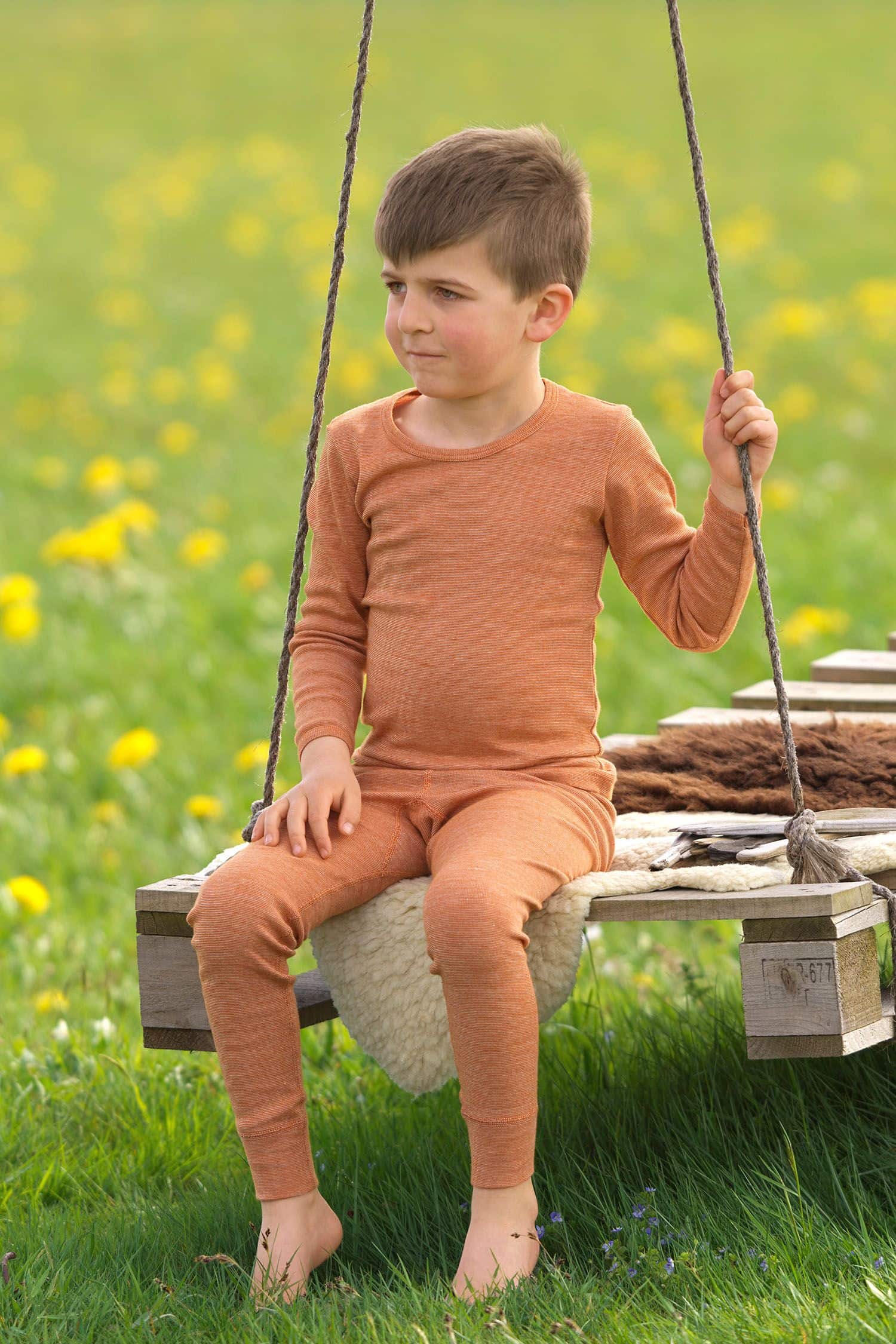 Junge sitzt auf Schaukel und trägt ein oranges Langarmshirt aus bio Wolle (kbT), bio Baumwolle (kbA) und Seide