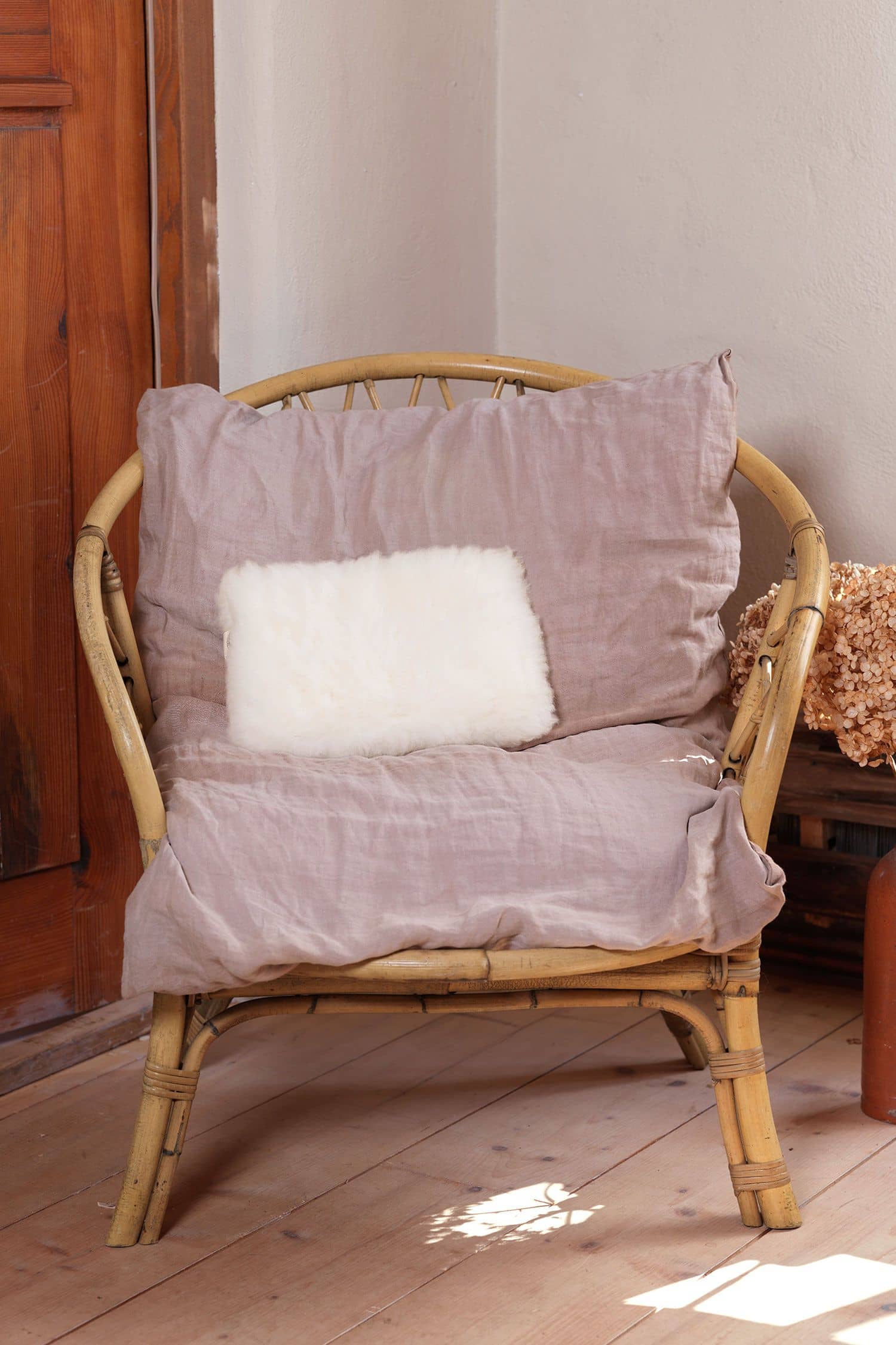 Kuschelkissen aus pflanzlich gegerbtem Finkhof Fell liegt auf einem Korbstuhl