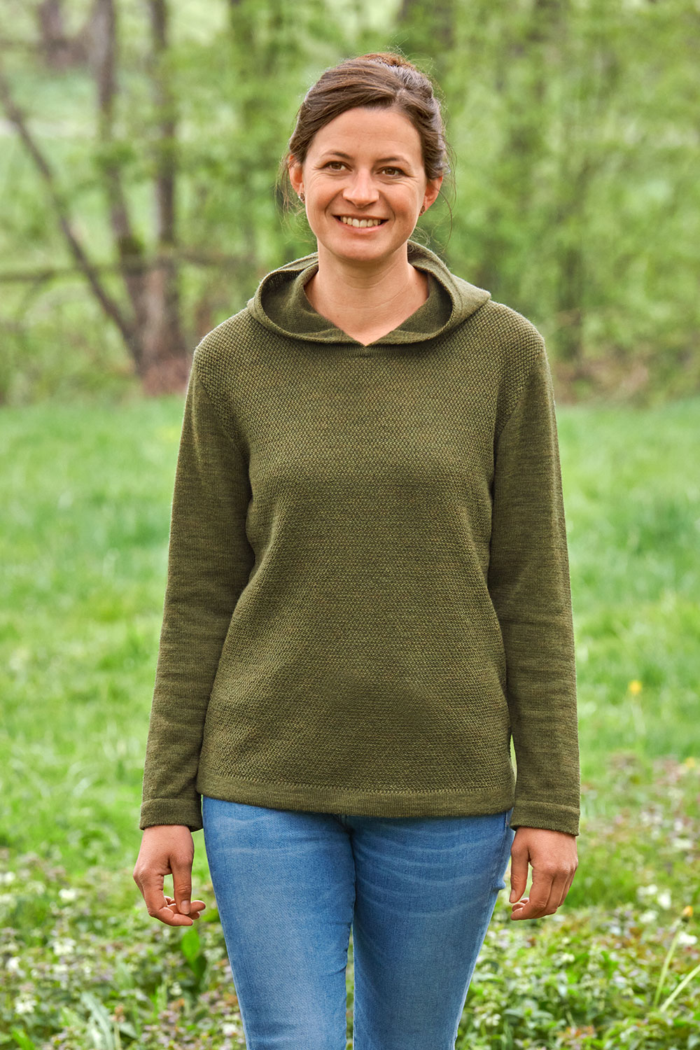 Frau auf Wiese trägt olivefarbener Kapuzenpulli vom Finkhof aus bio Wolle (kbT)