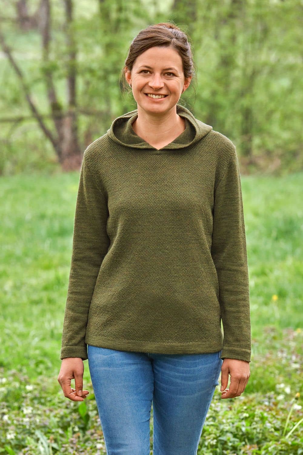 Frau auf Wiese trägt olivefarbener Kapuzenpulli vom Finkhof aus bio Wolle (kbT)