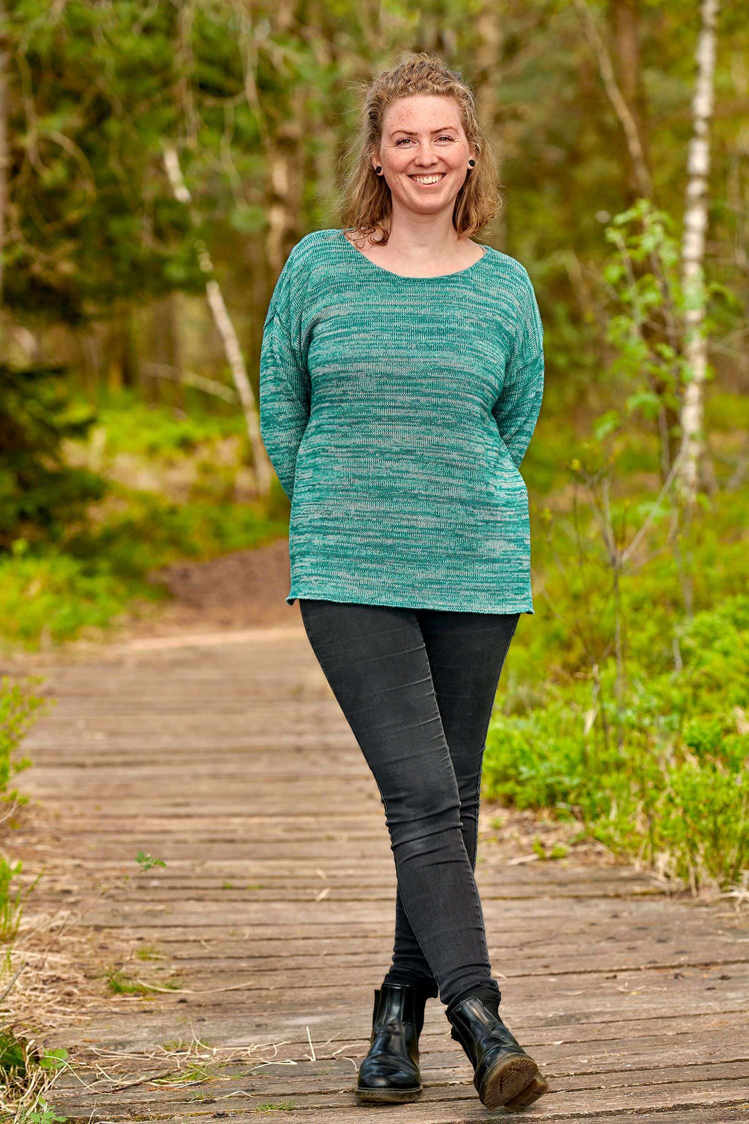 Frau mit schwarzer Jeans trägt einen türkisen Oversize Strickpullover aus bio Baumwolle (kbA) und bio Wolle (kbT)