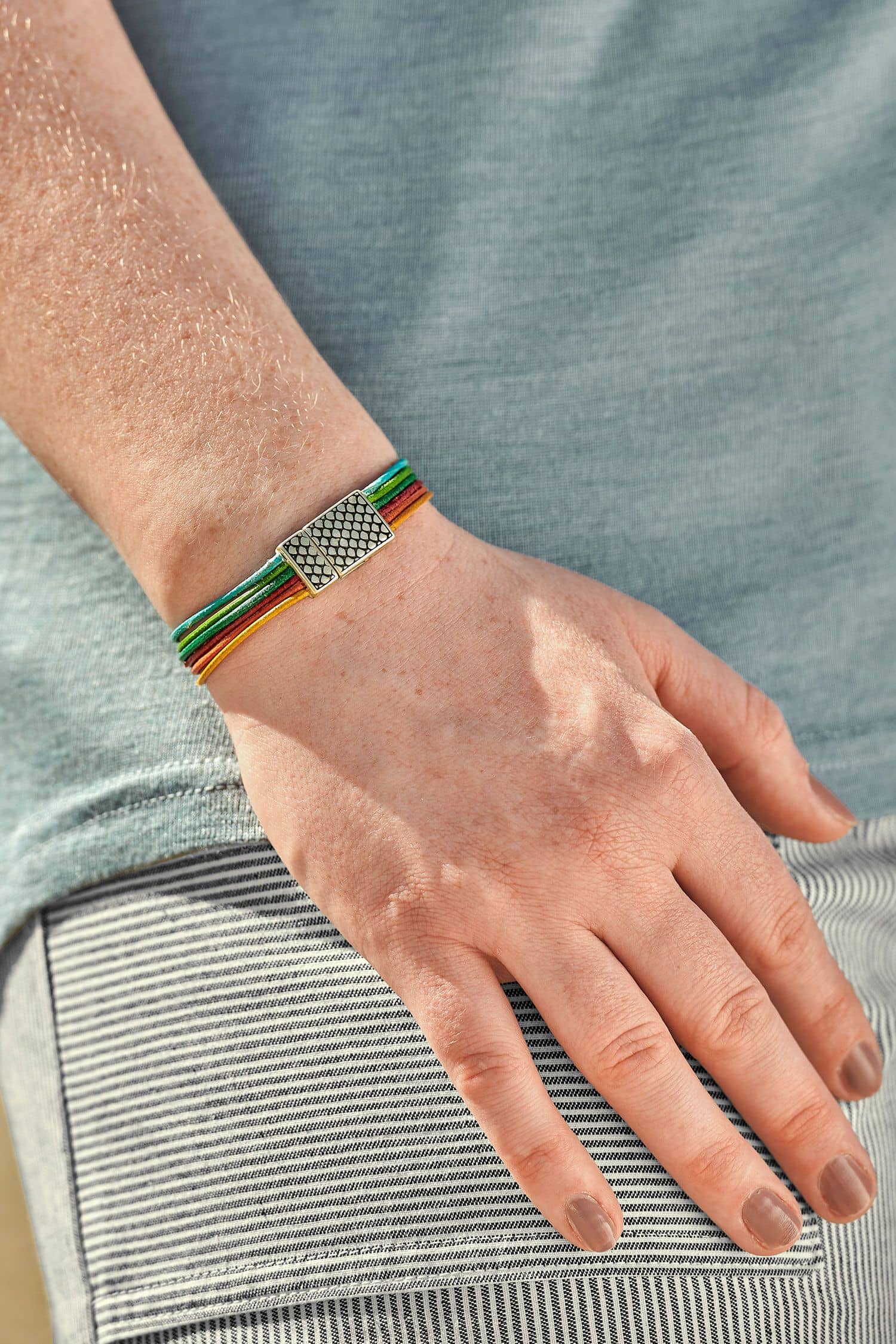 Frau mit blauem Shirt trägt kunterbuntes Lederarmband aus Rinds- und Ziegenleder mit silberfarbenem Verschluss