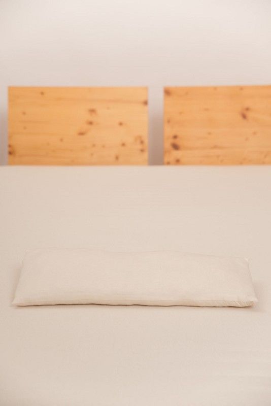 Finkhof Lendenkissen mit 20x50cm aus bio Wolle (kbT) und bio Baumwolle (kbA) auf braunem Bett mit hellem Laken