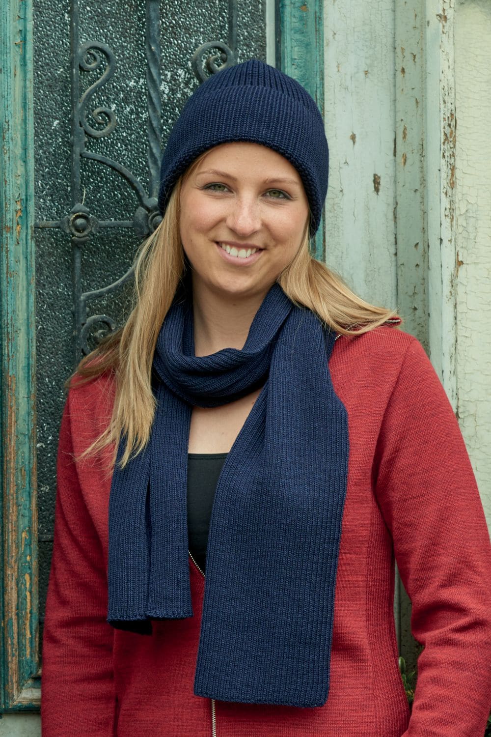 Frau mit roter Weste trägt eine dunkelblaue Mütze und einen marineblauen Strickschal aus bio Wolle (kbT) vom Finkhof
