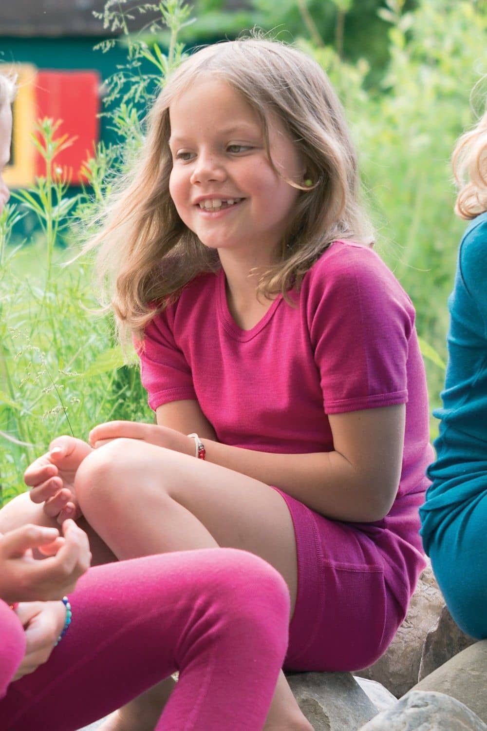 Wolle-Seide Kurzarmshirt fuchsia Gr. 152 Rundhals Mädchen sitzt auf Steinen und trägt pinkes Kurzarmshirt aus bio Wolle (kbT) und Seide