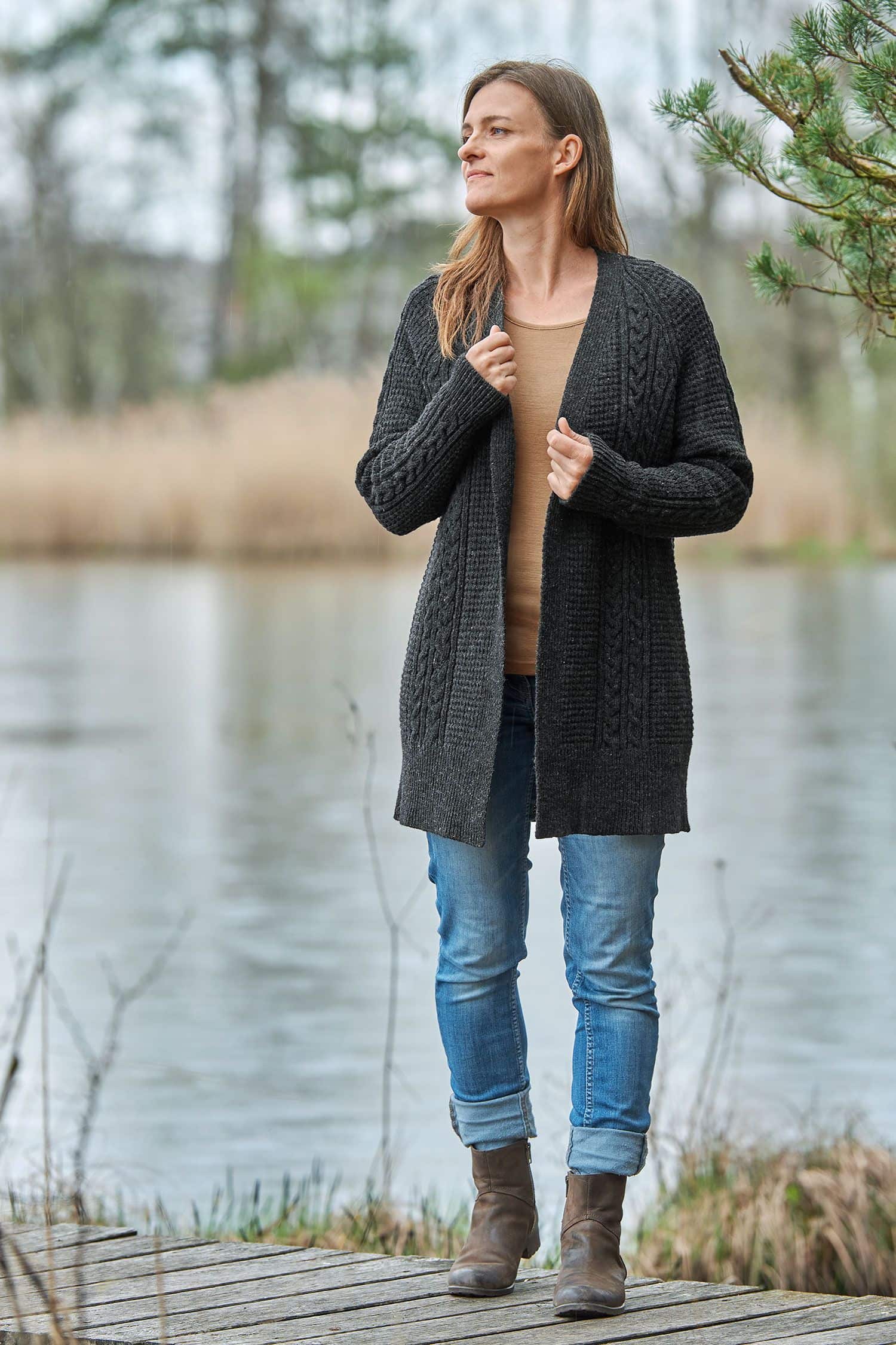 Frau auf Steg trägt anthrazitfarbenen Cardigan vom Finkhof mit Zopfmuster aus bio Wolle (kbT) , unifarbiges Shirt und Jeans