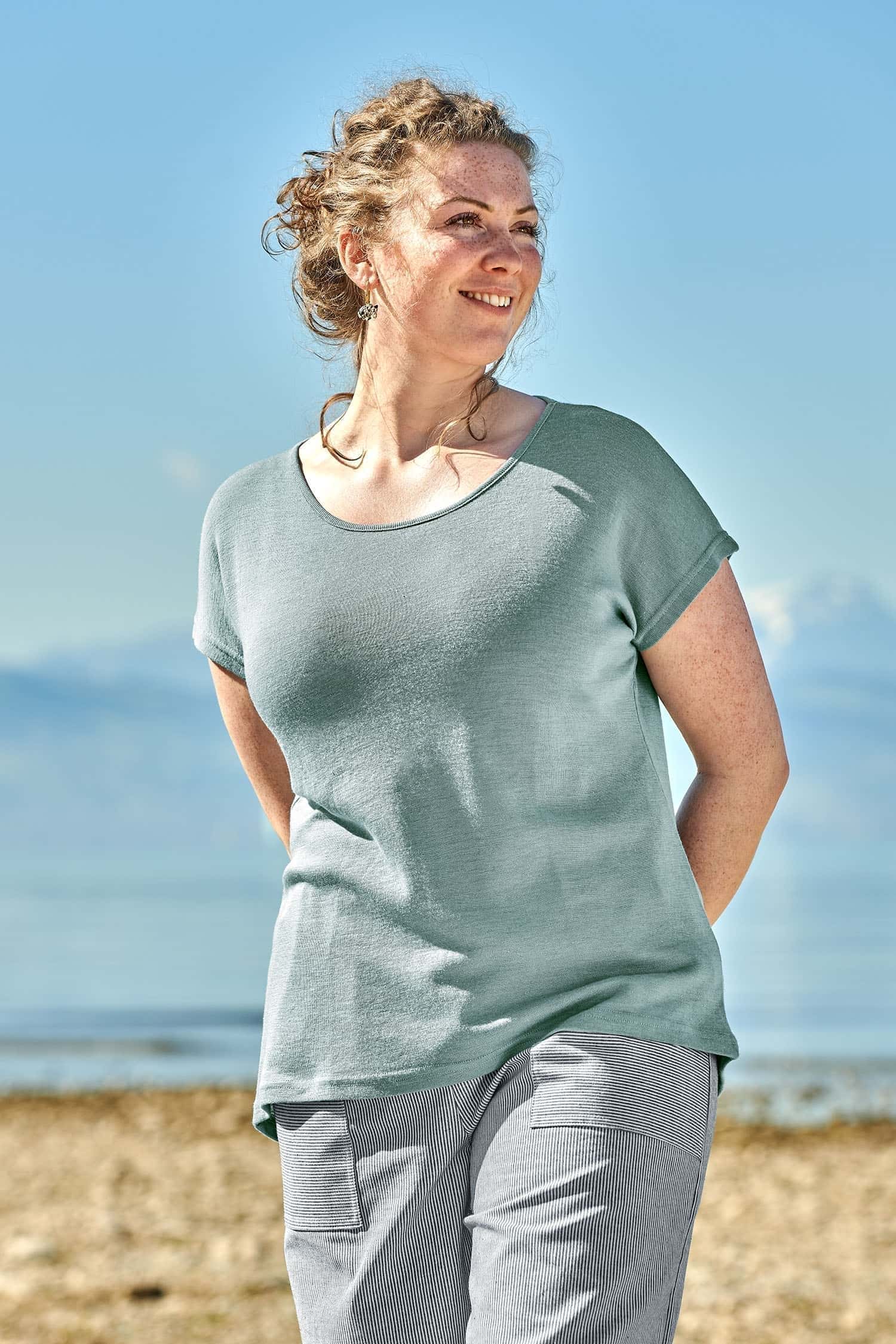 Lachende Frau mit blau weiß gestreifter Hose trägt ein pastellblaues Oversize Shirt aus Bio-Wolle und Seide mit GOTS