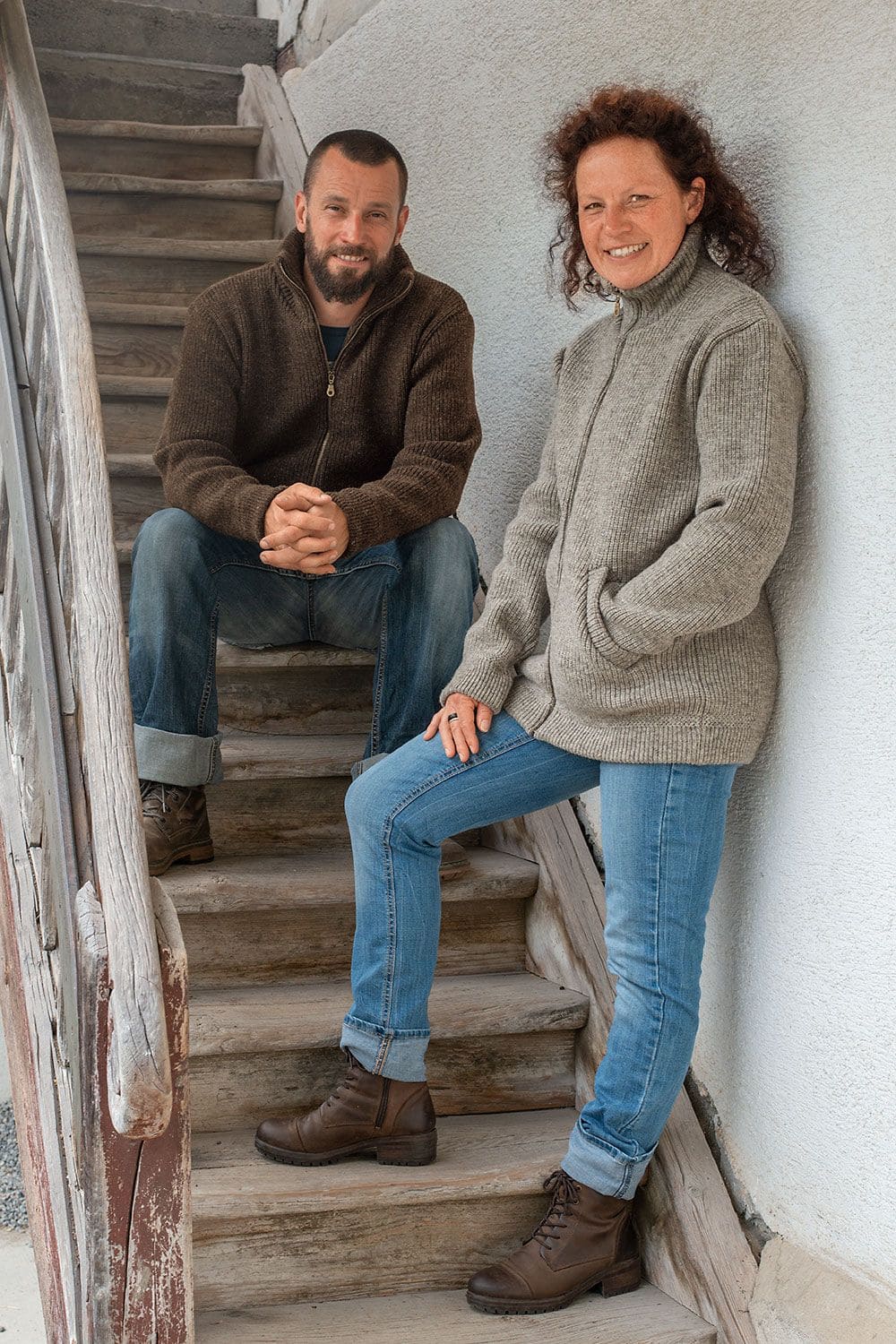 Finkhof-Jacke Frau und Mann auf Treppe tragen graue und braune Finkhof Jacke aus bio Wolle (kbT) mit Stehkragen