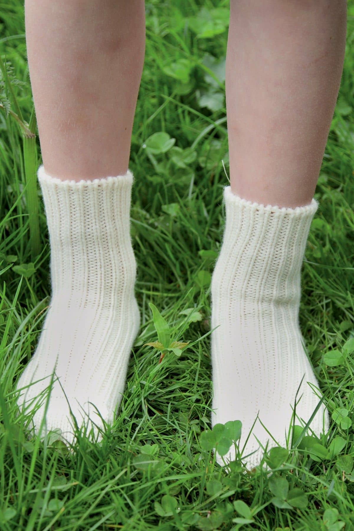 Kind mit naturweißen Wollsocken aus bio Wolle (kbT) steht auf einer Wiese