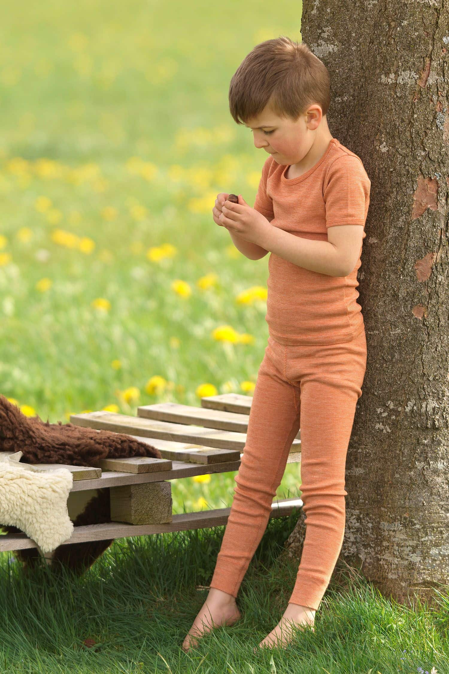 Junge lehnt an Baum und trägt orange lange Unterhose aus bio Wolle (kbT), bio Baumwolle (kbA) und Seide mit passendem Shirt