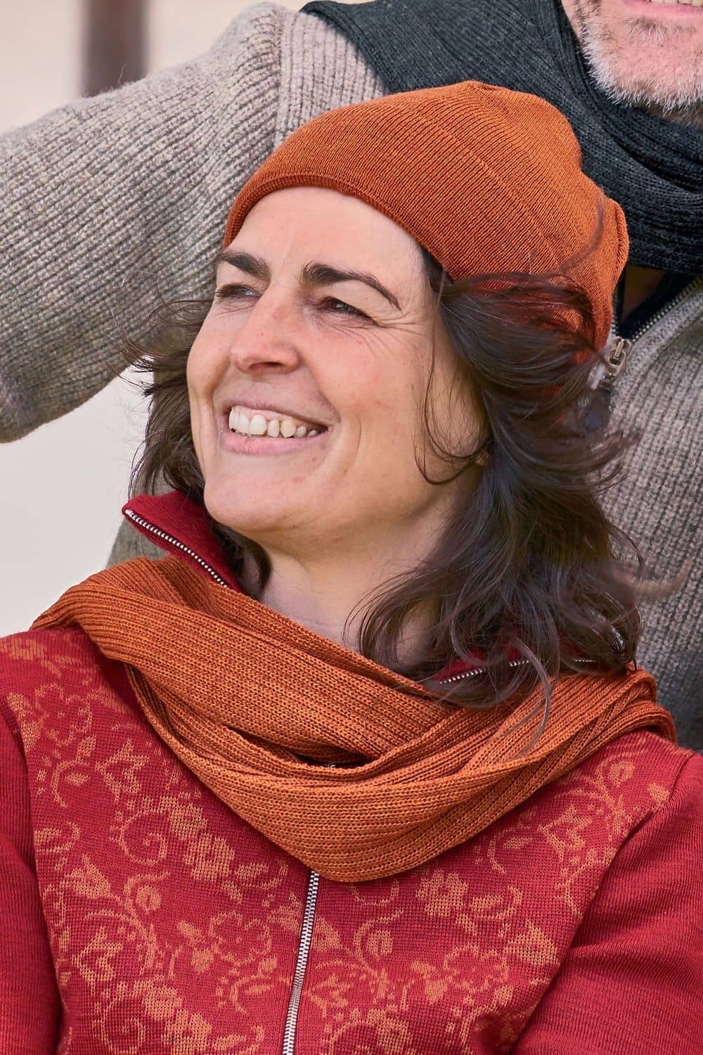 Frau mit roter Jacke trägt orange leichte Mütze aus bio Wolle (kbT) und bio Baumwolle (kbA) vom Finkhof und einen Schal