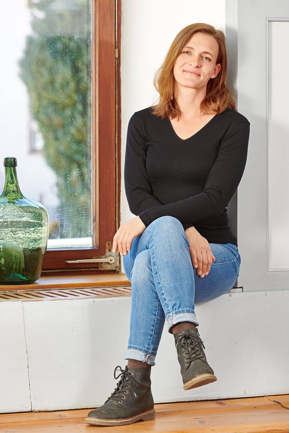 Frau sitzt auf Fensterbank und trägt ein schwarzes Langarmshirt aus bio Wolle (kbT) und Seide mit V Ausschnitt