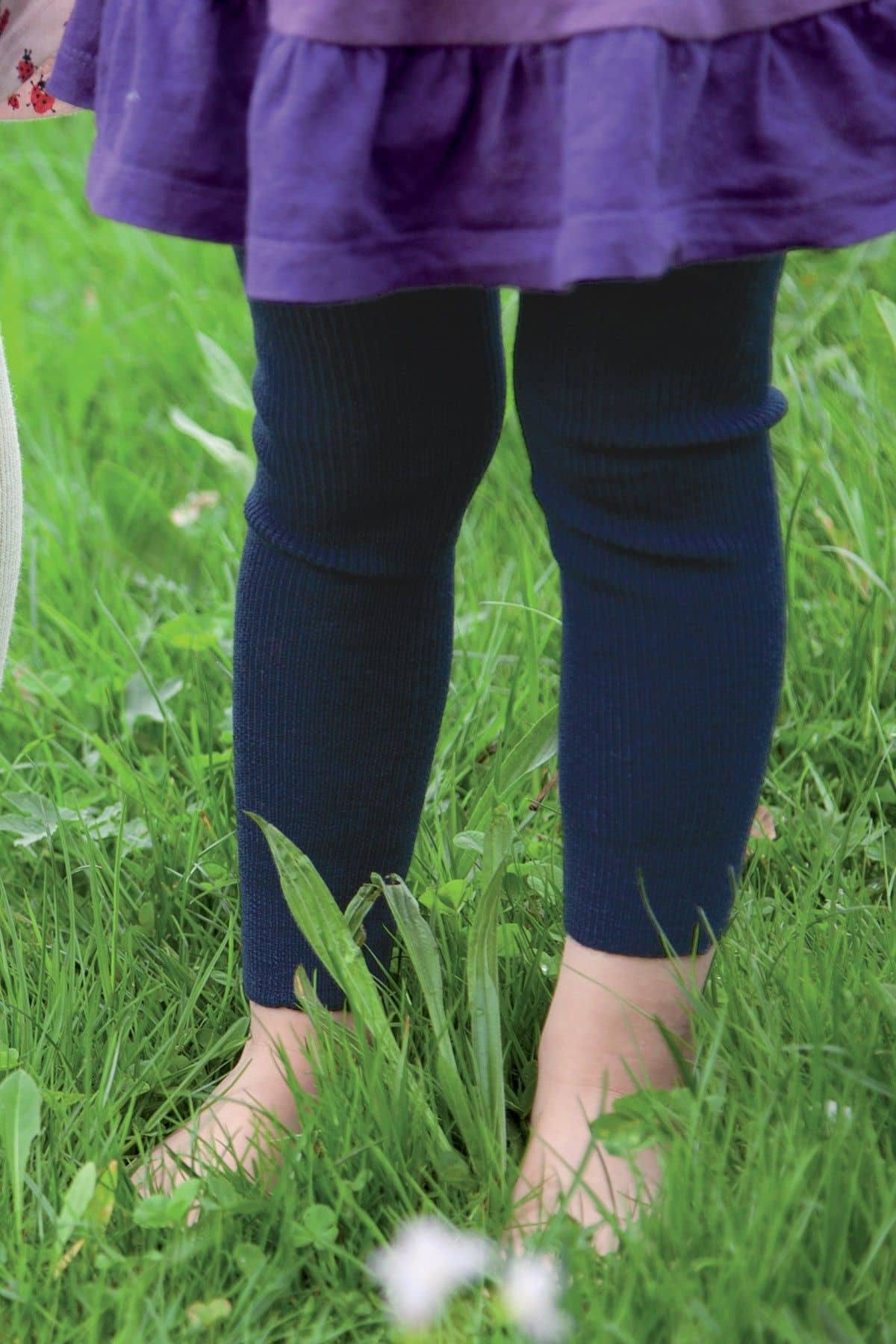 Kind steht auf einer Wiese und trägt eine marineblaue Leggings aus bio Wolle (kbT)) und ein lila Kleid