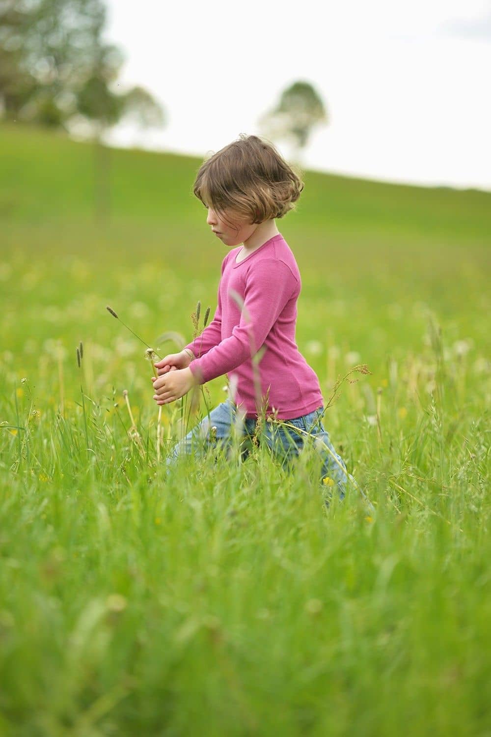 Kind trägt fuchsiafarbenes Wolle Seide Langarmshirt aus bio Wolle (kbT) und spielt dabei auf Wiese