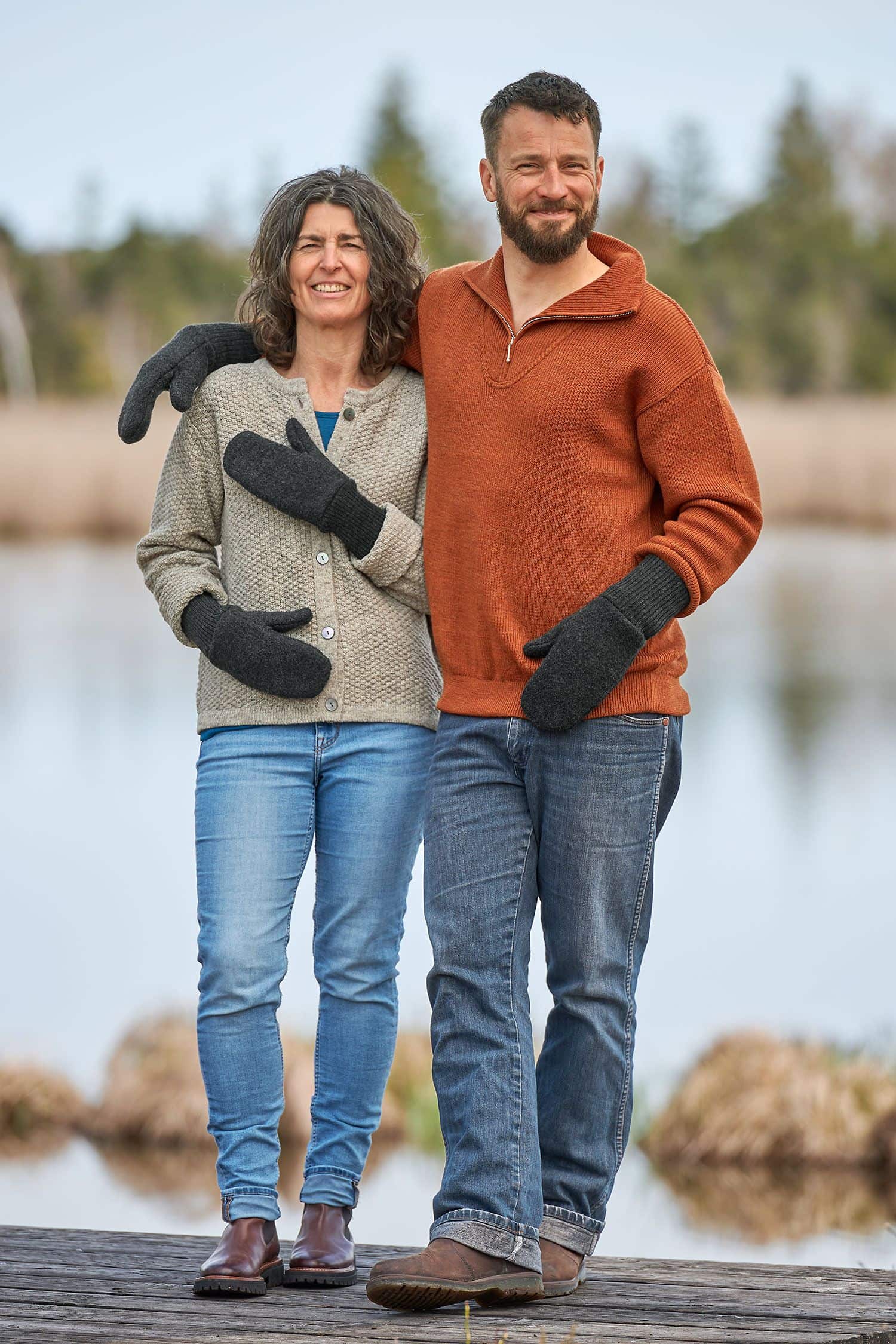 Mann und Frau mit Strickpullis tragen graue Fäustlinge aus bio Wolle (kbT) vom Finkhof und stehen auf einem Steg