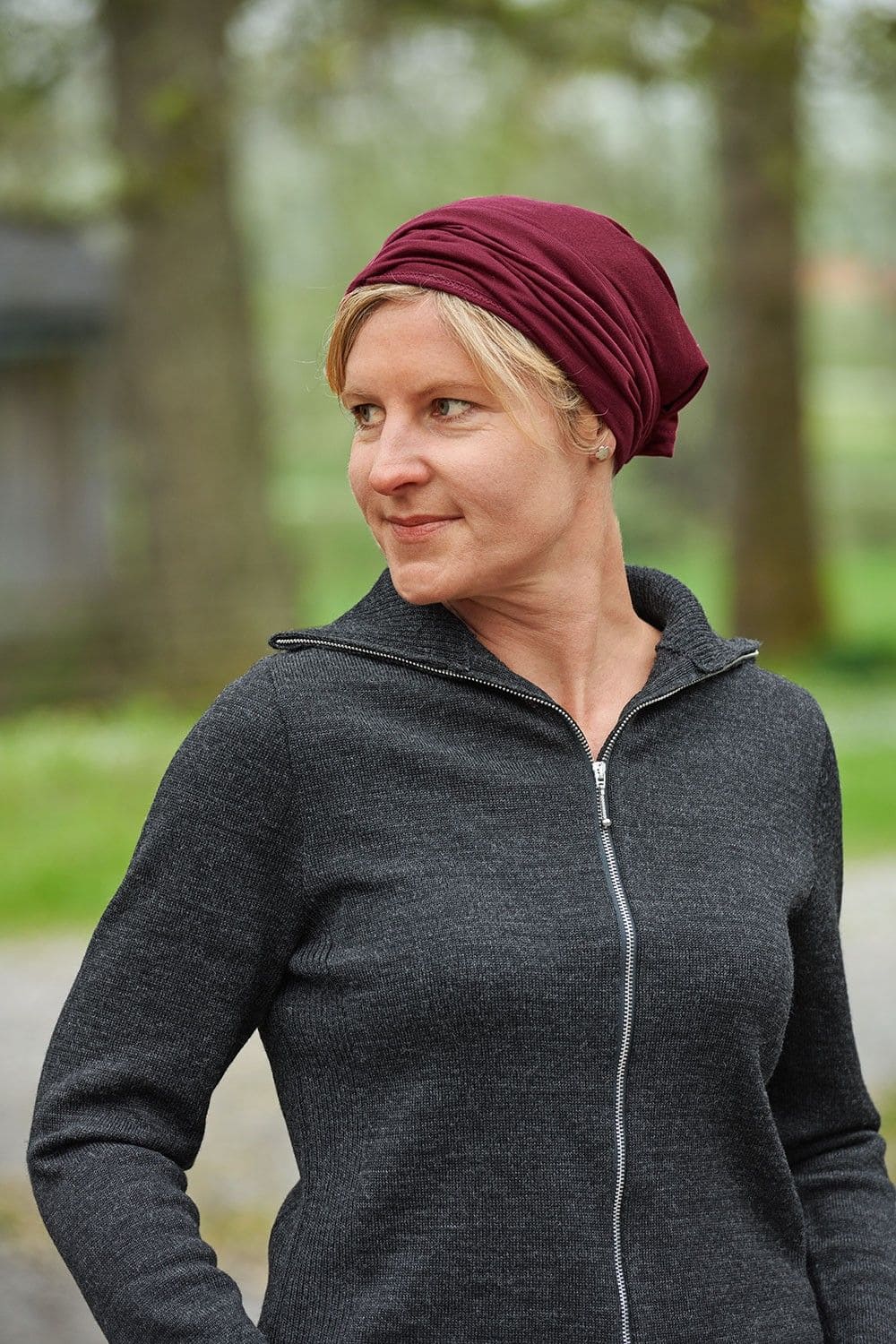 Frau mit grauer Weste trägt einen bordeauxroten Sportschal aus bio Wolle (kbT) und Seide als Mütze